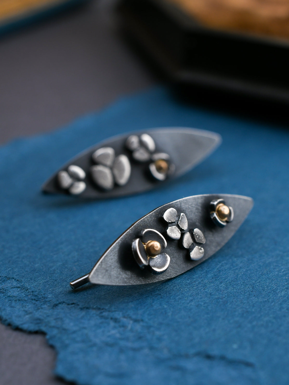 Silver leaf-shaped earrings with floral designs on a blue surface
