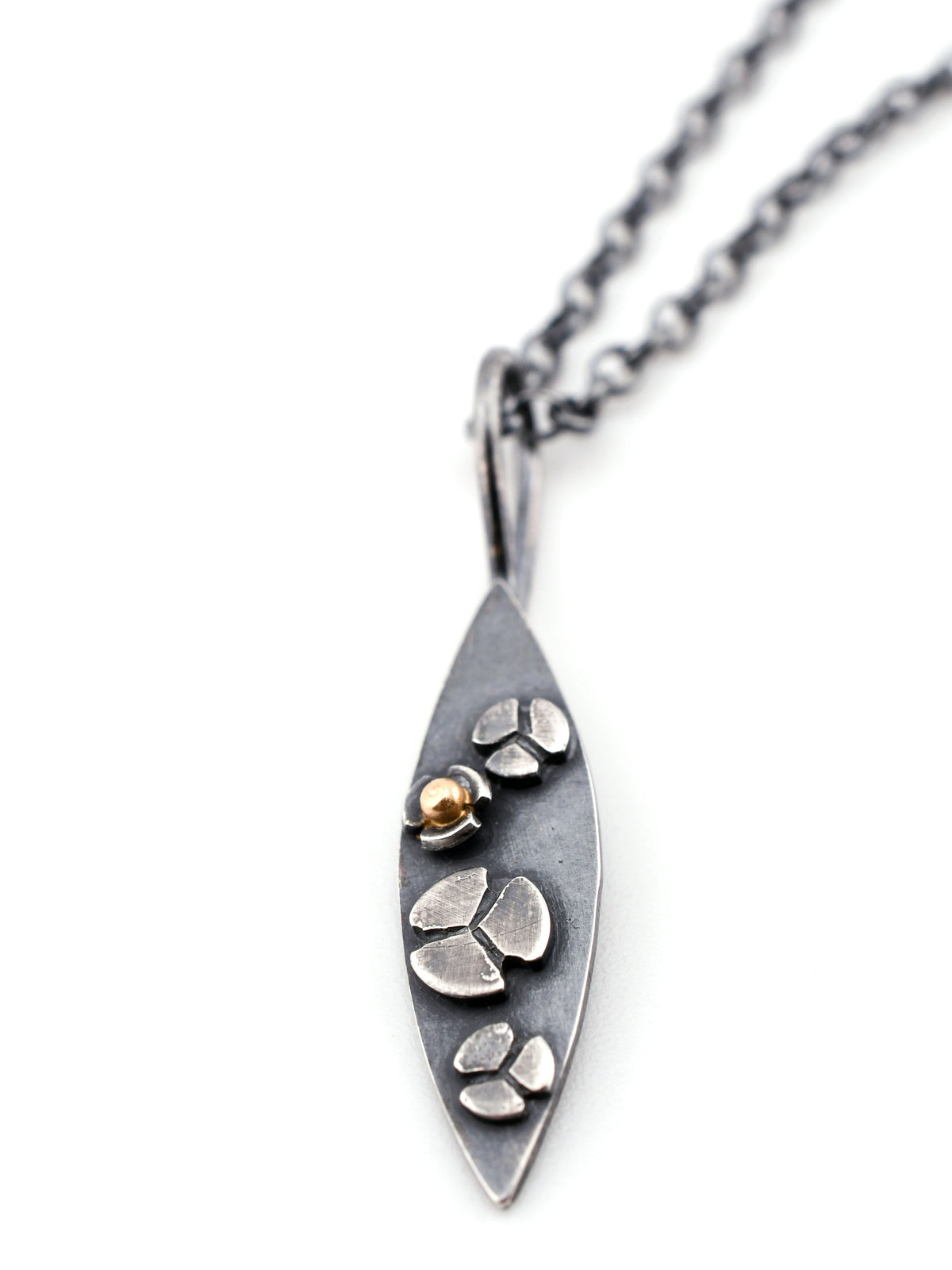 Closeup of a marquis-shaped pendant with stylized flowers, one with a 14k gold center, on a white surface