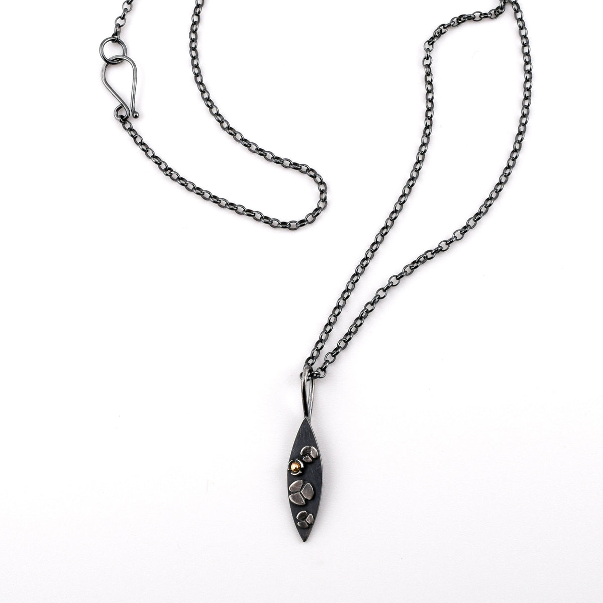 A necklace with a marquise shaped pendant featuring three lobed flowers on the surface, one with a 14k gold center, on a white background
