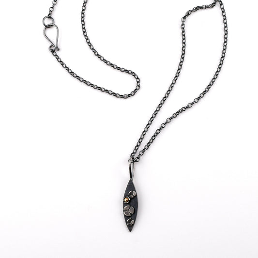 A necklace with a marquise shaped pendant featuring three lobed flowers on the surface, one with a 14k gold center, on a white background