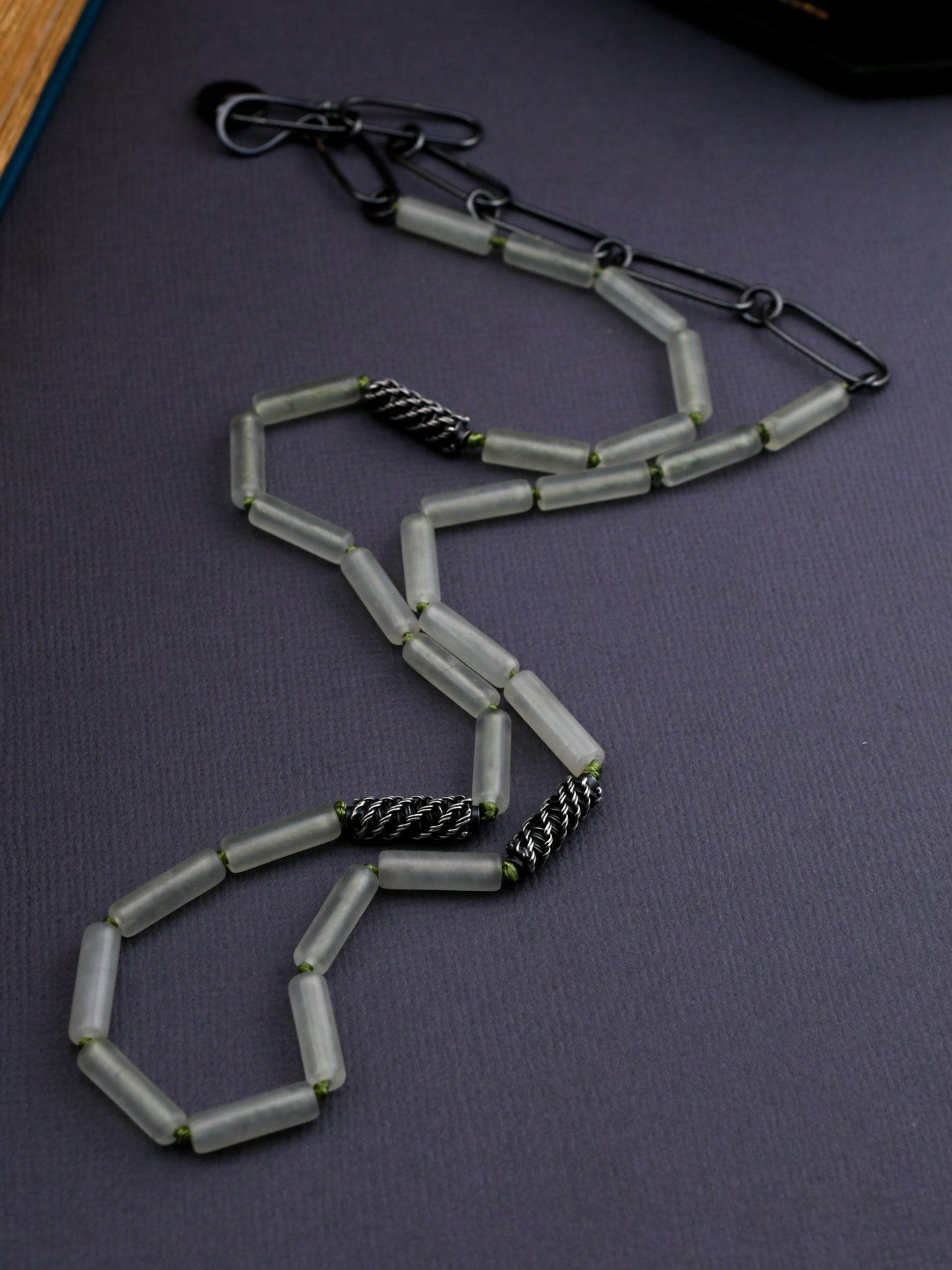 Pale green bead necklace with textured silver beads on a dark gray background