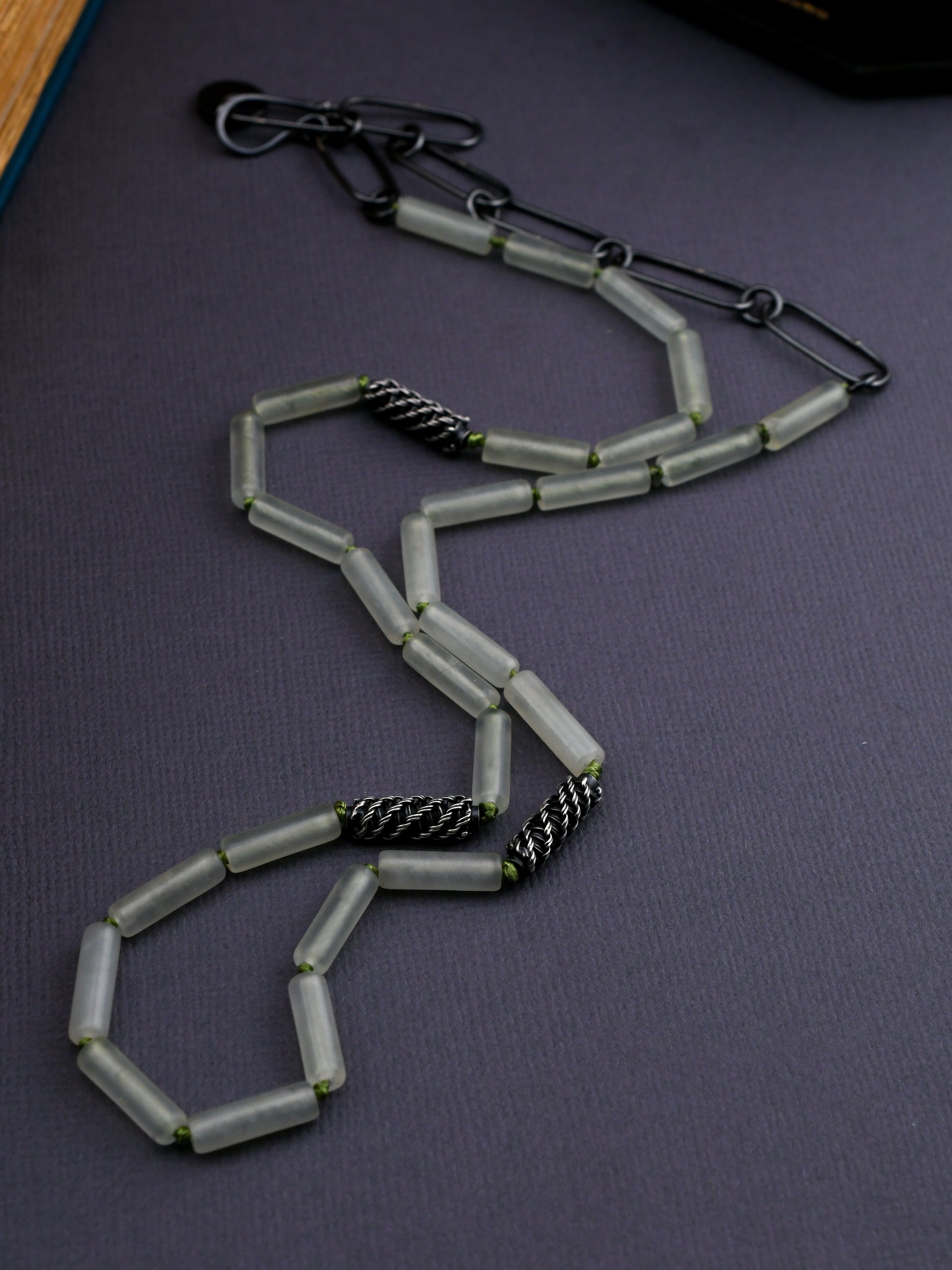Pale green bead necklace with textured silver beads on a dark gray background