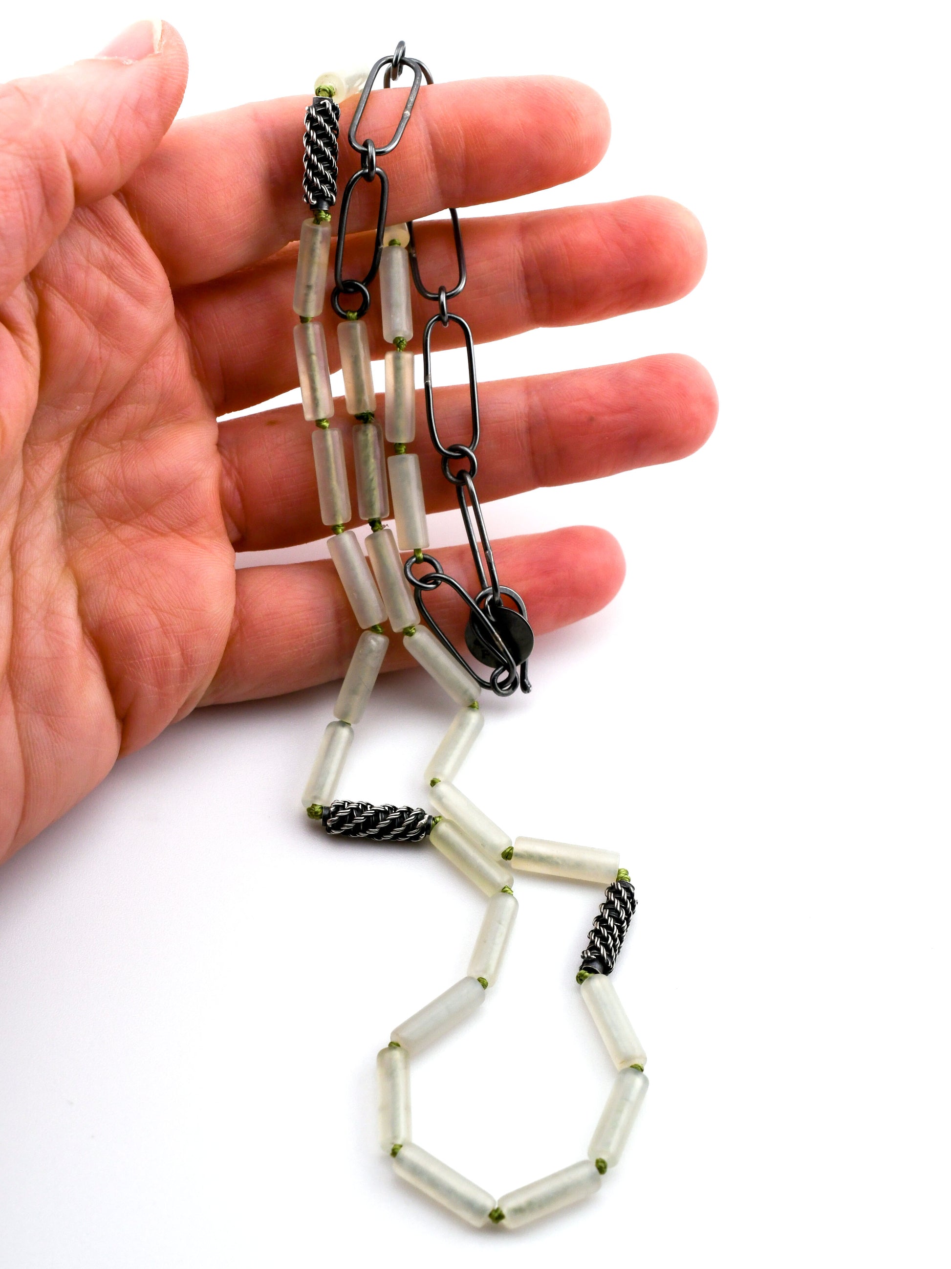 cylindrical green bead and woven silver bead necklace held in a hand on a white background