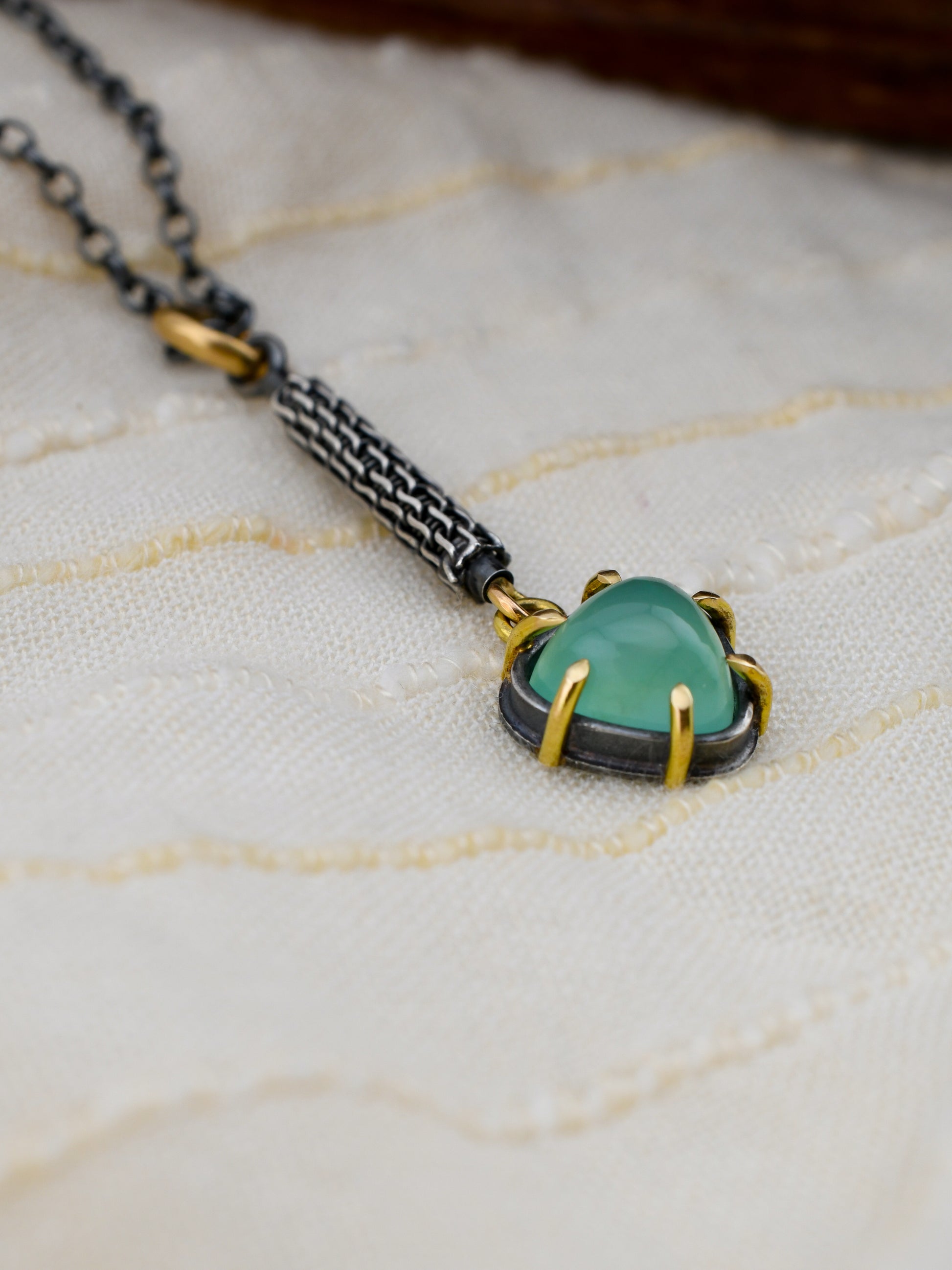 Necklace with a green gemstone pendant on a textured fabric background