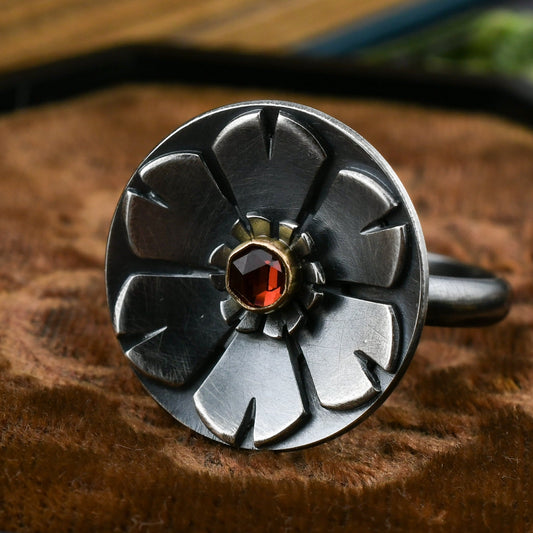 Helios ring in blackened sterling silver with garnet set in 14k gold displayed on brown velvet with a blurred background