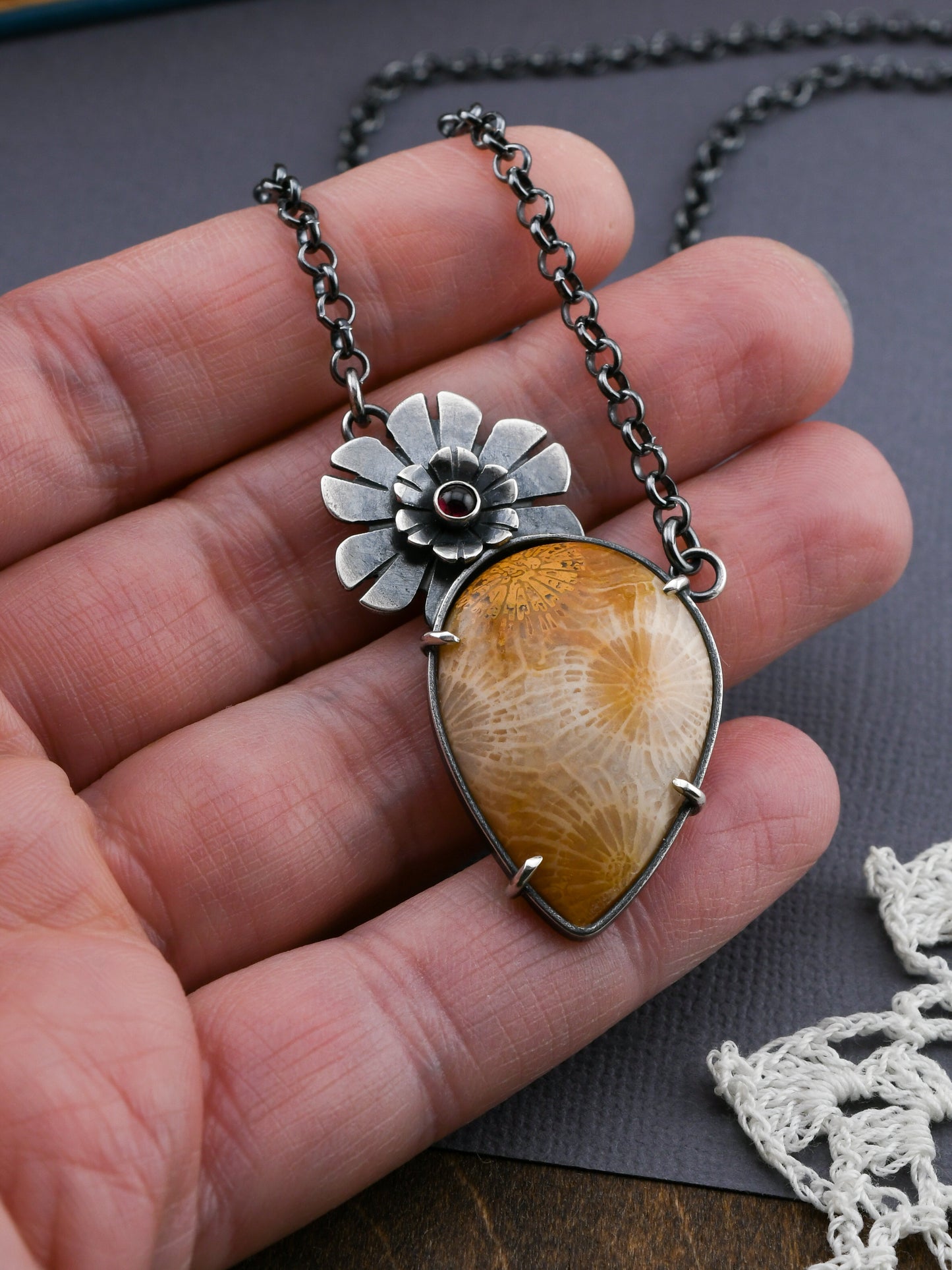 Necklace with a floral pendant and golden fossil coral stone held in a hand on a gray surface.
