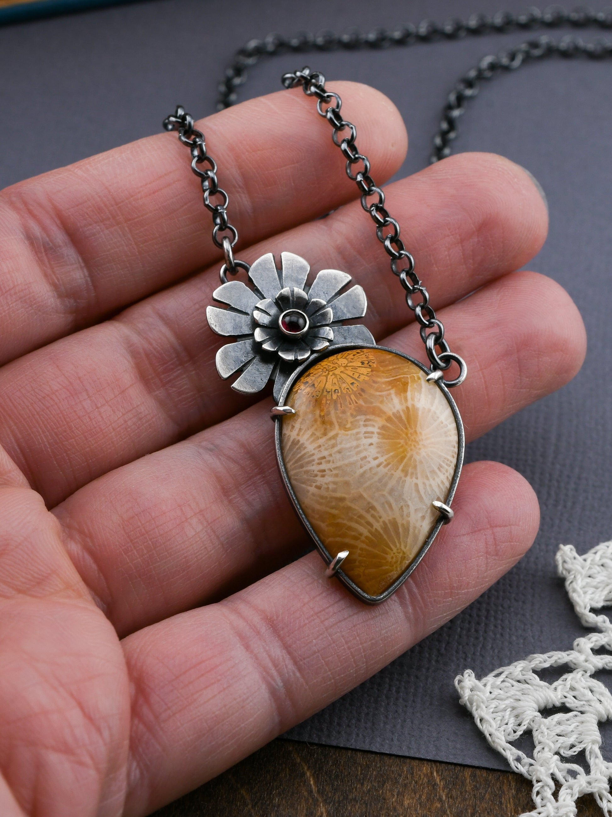 Necklace with a floral pendant and golden fossil coral stone held in a hand on a gray surface.