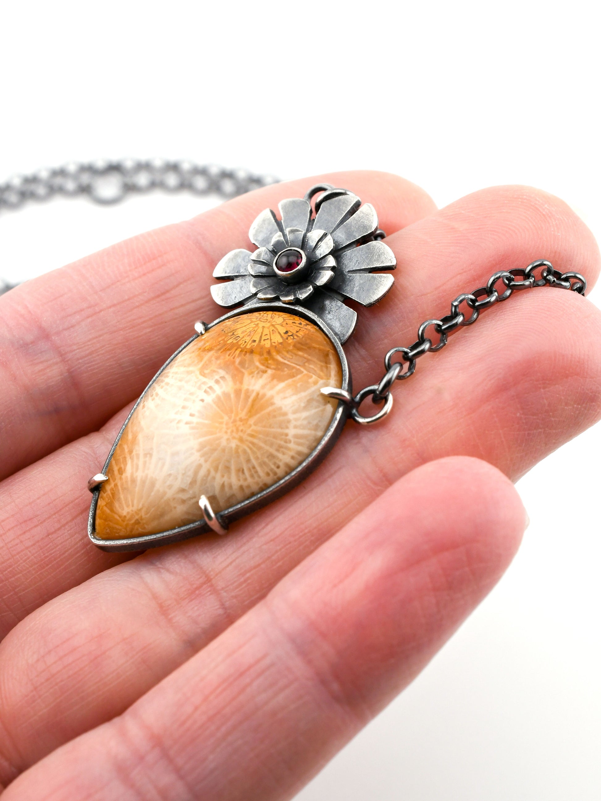 Hand holding a unique necklace with a floral design and amber-colored stone.