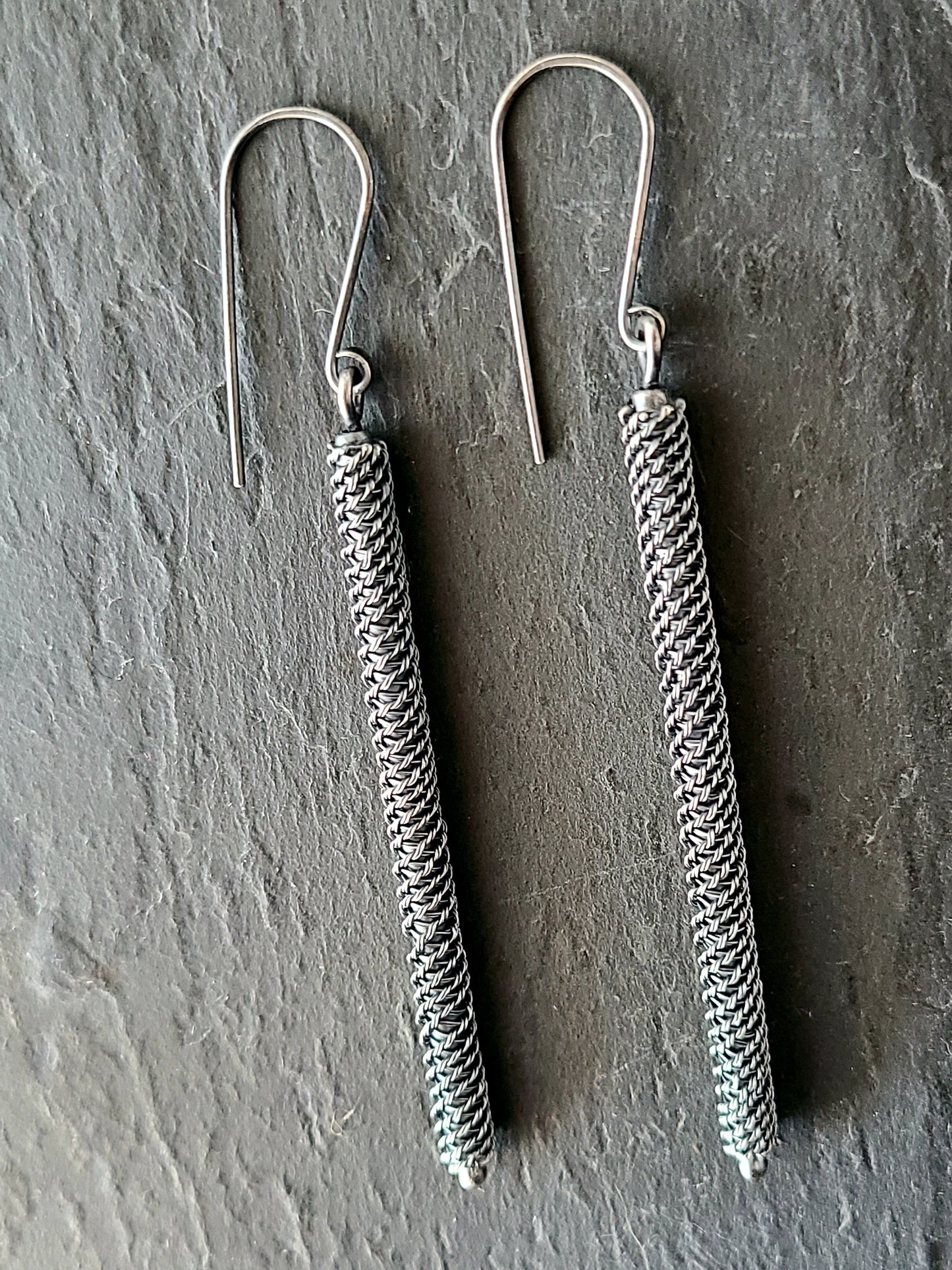 Long black earrings with twisted wire pattern on a textured black background