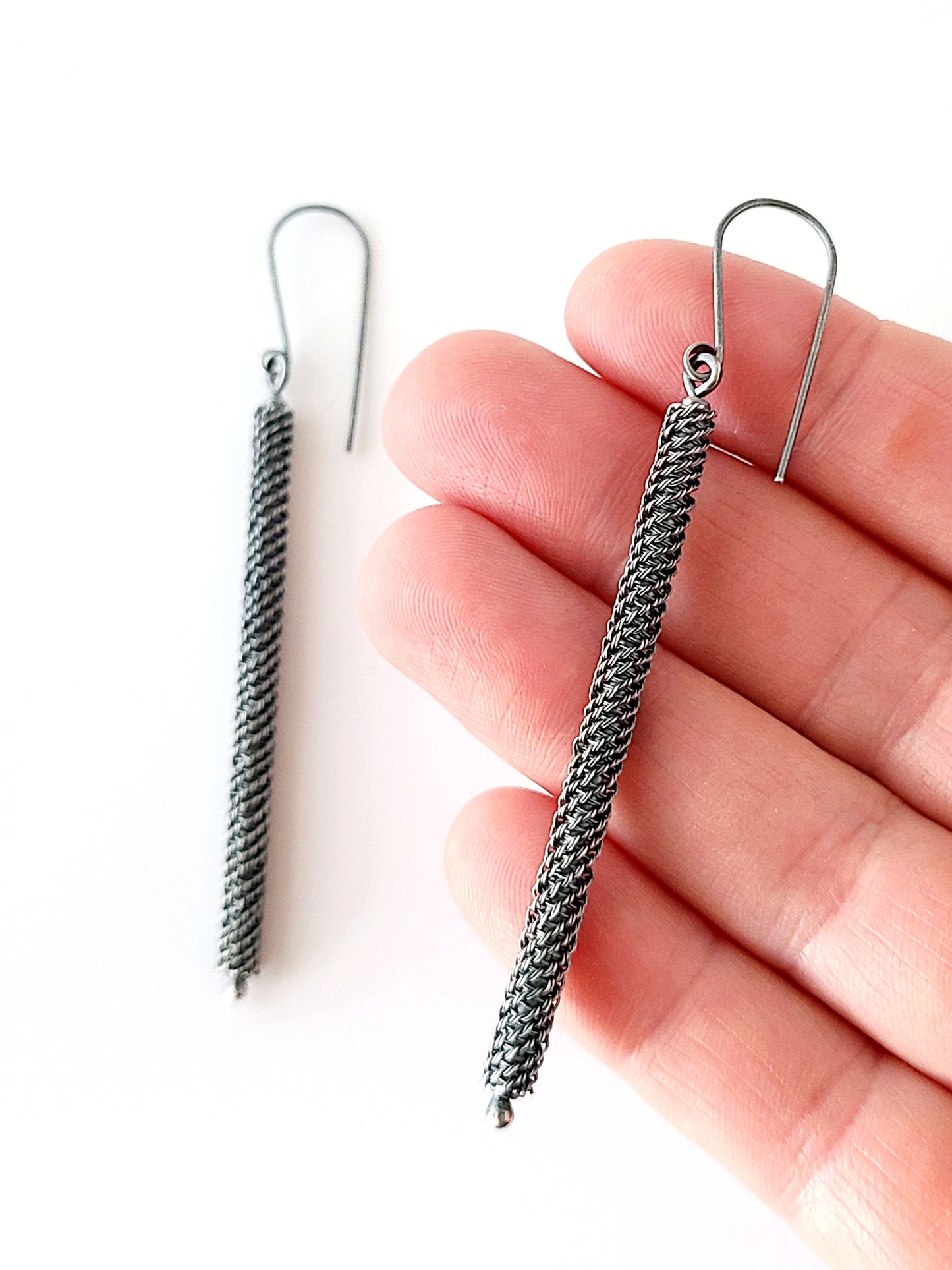 Silver braided earrings held between fingers on a white background