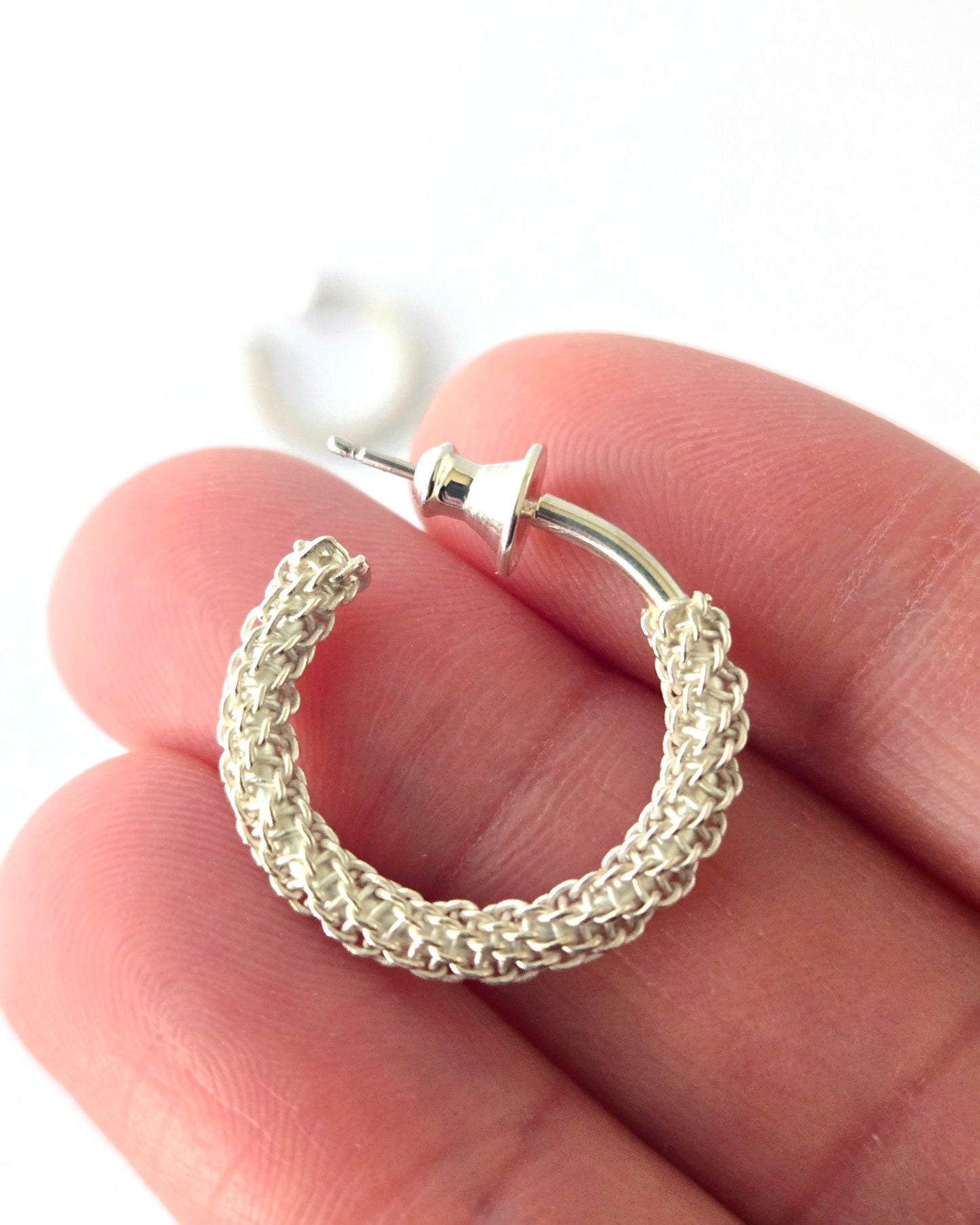 Silver hoop earring held between fingers on a white background