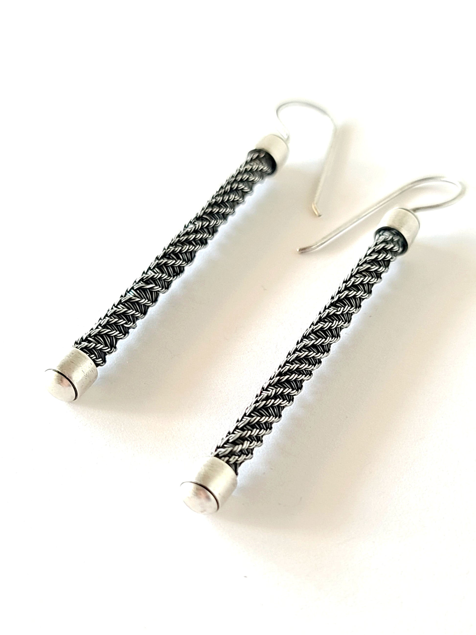Pair of silver earrings with braided design on a white background