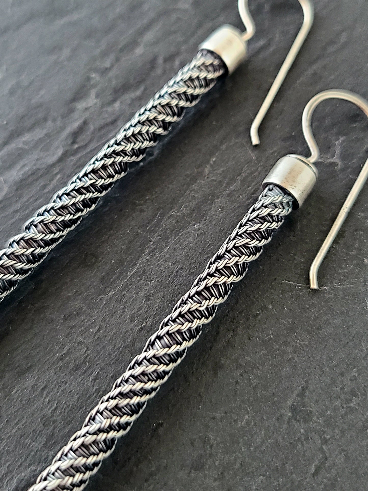 closeup of long silver earrings with twisted wire pattern on a black background