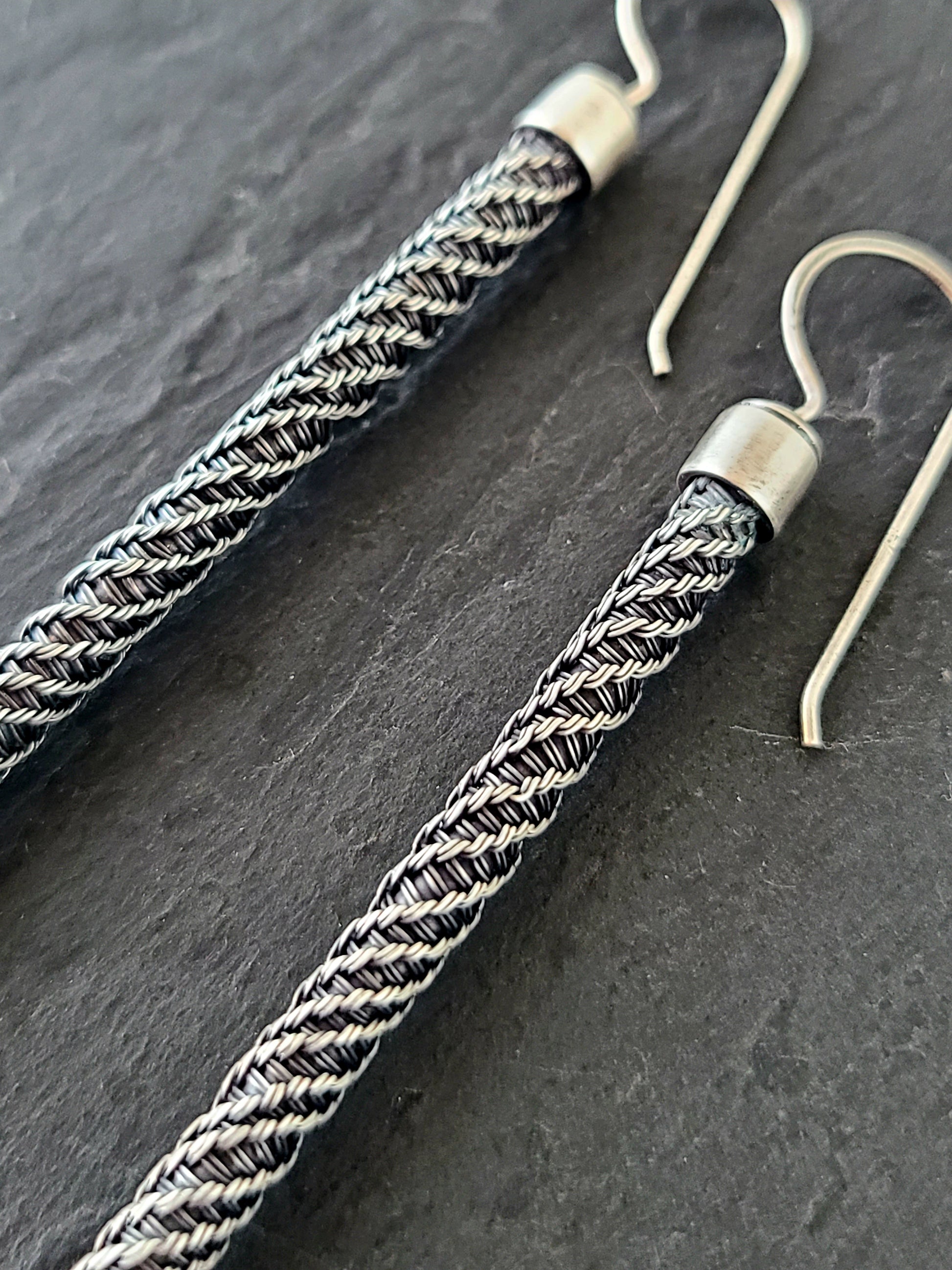 closeup of long silver earrings with twisted wire pattern on a black background