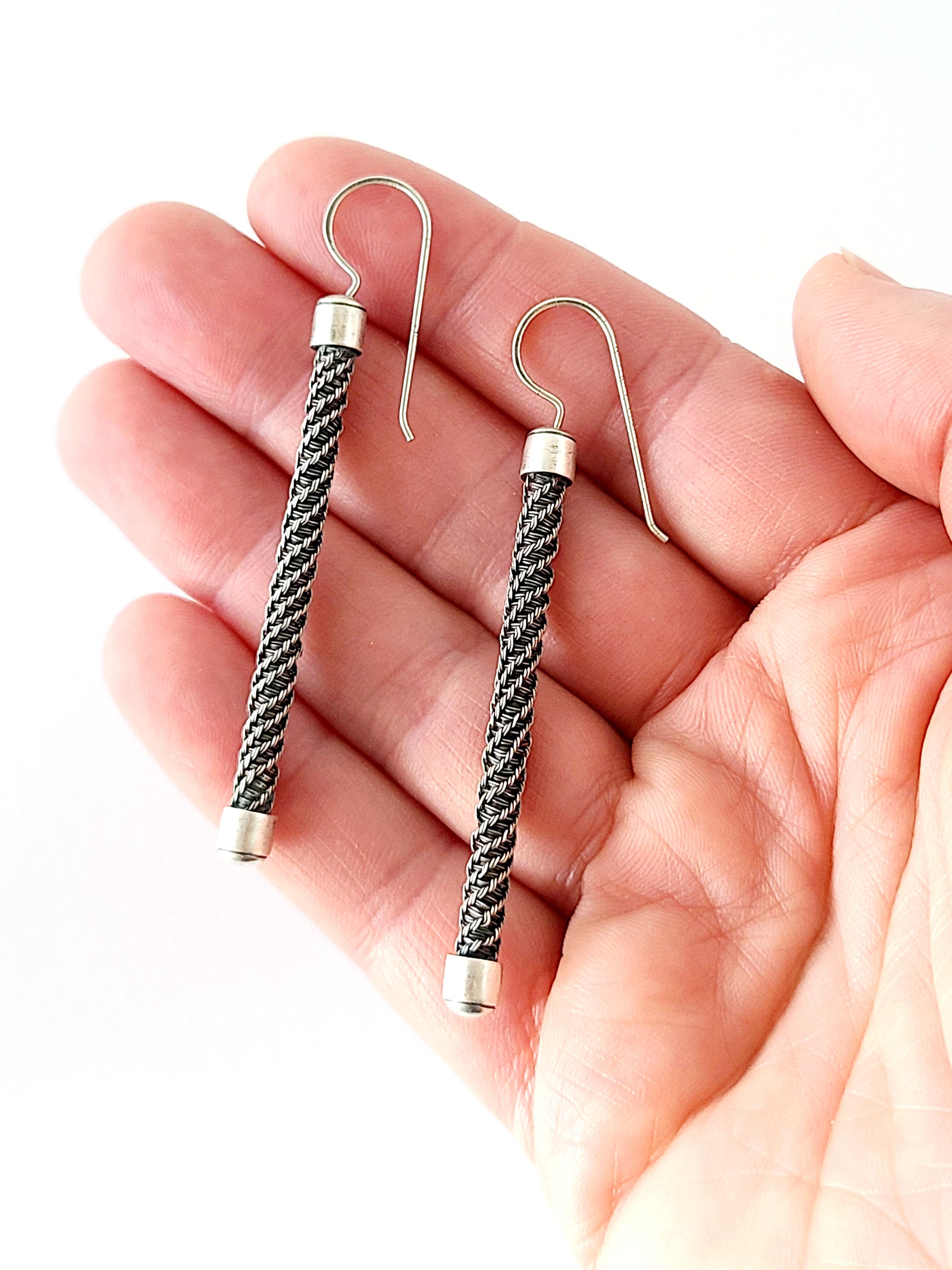 Pair of braided wire earrings held in a hand against a white background