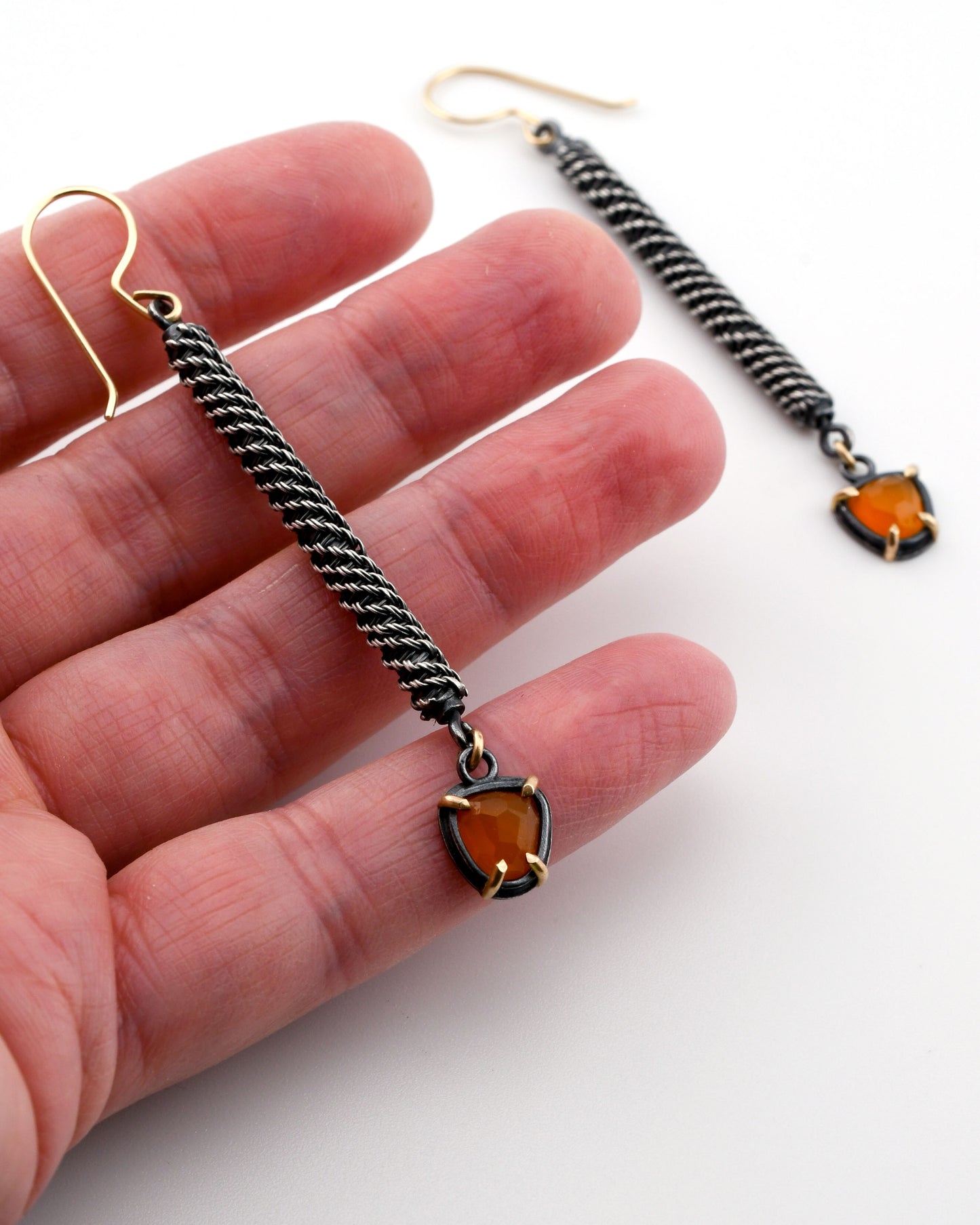 Pair of earrings with orange gemstones held between fingers on a white background