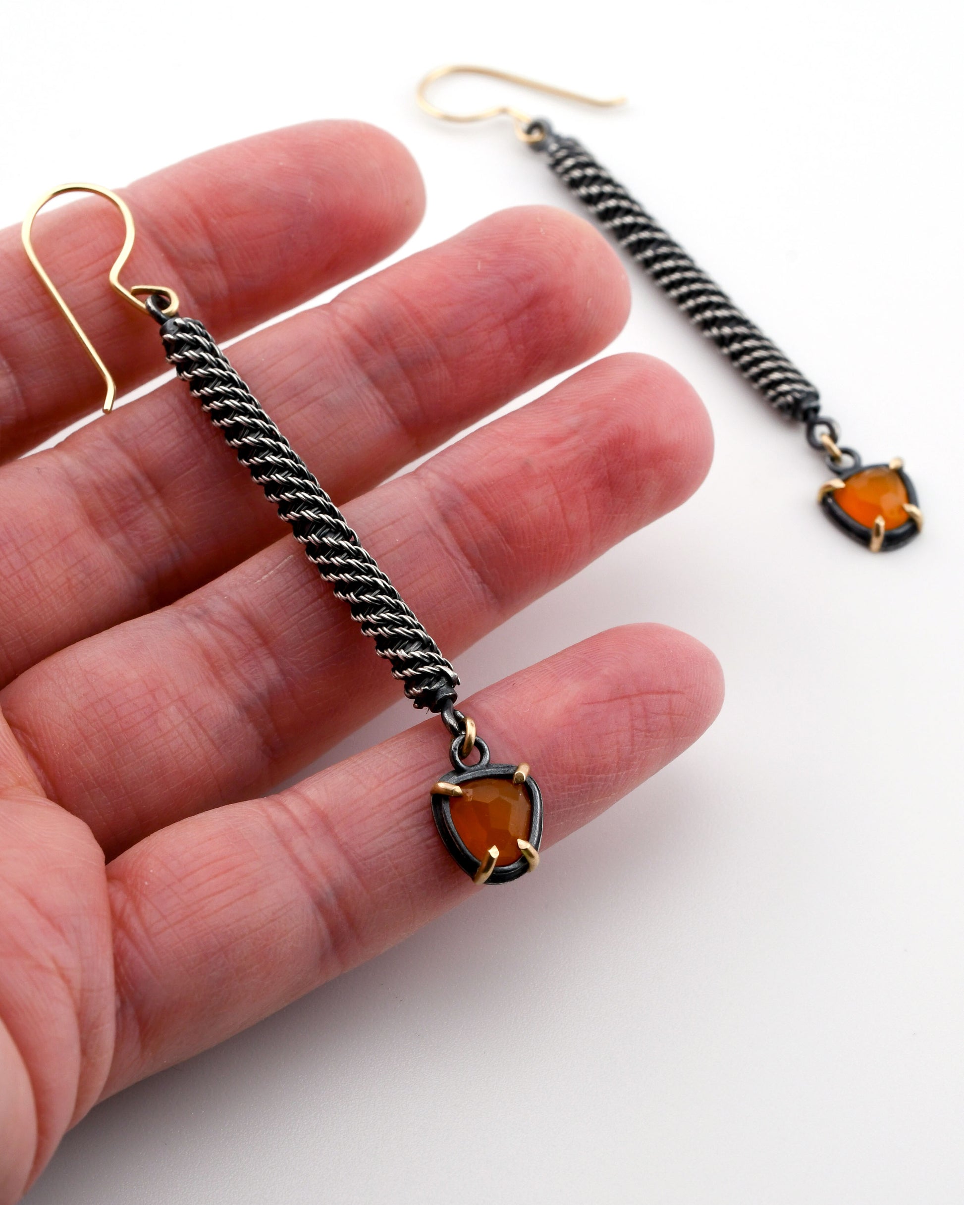 Pair of earrings with orange gemstones held between fingers on a white background