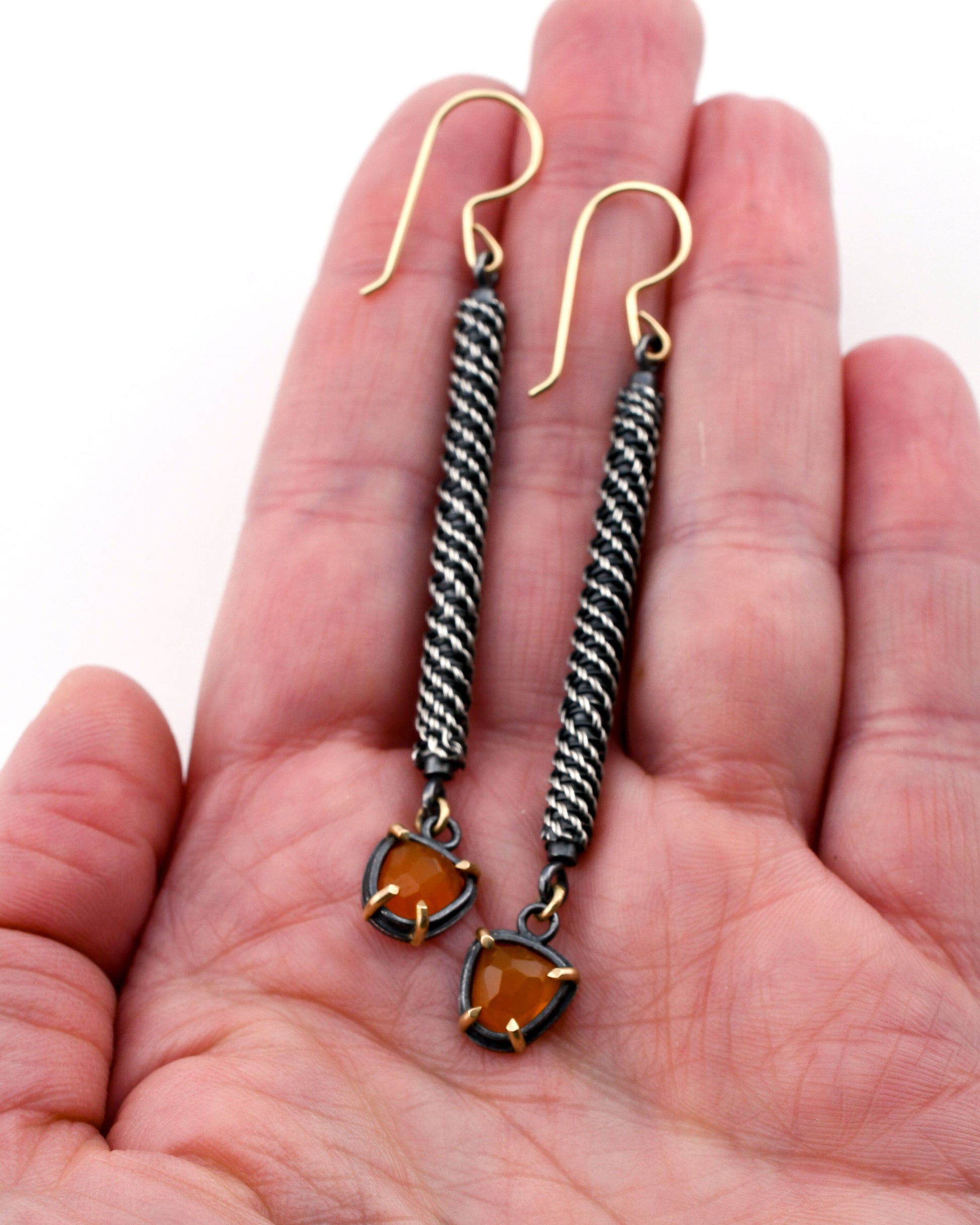 Pair of silver and carnelian earrings held in a hand against a white background
