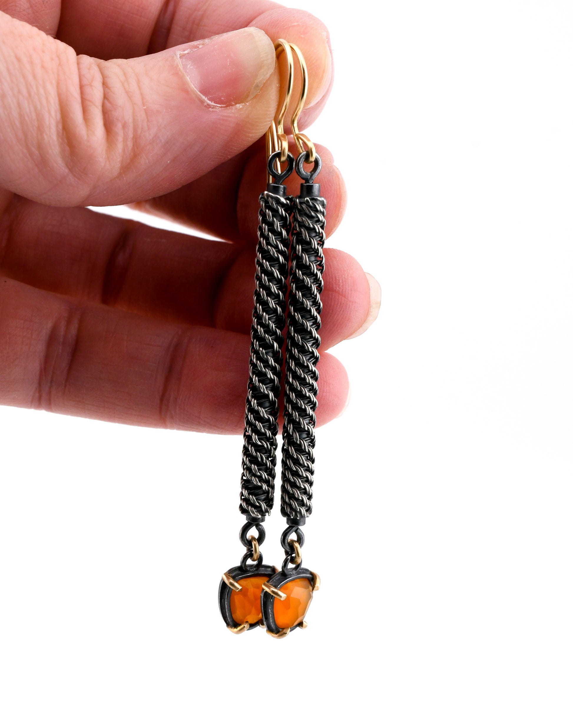 Hand holding a pair of earrings with orange and black design on a white background