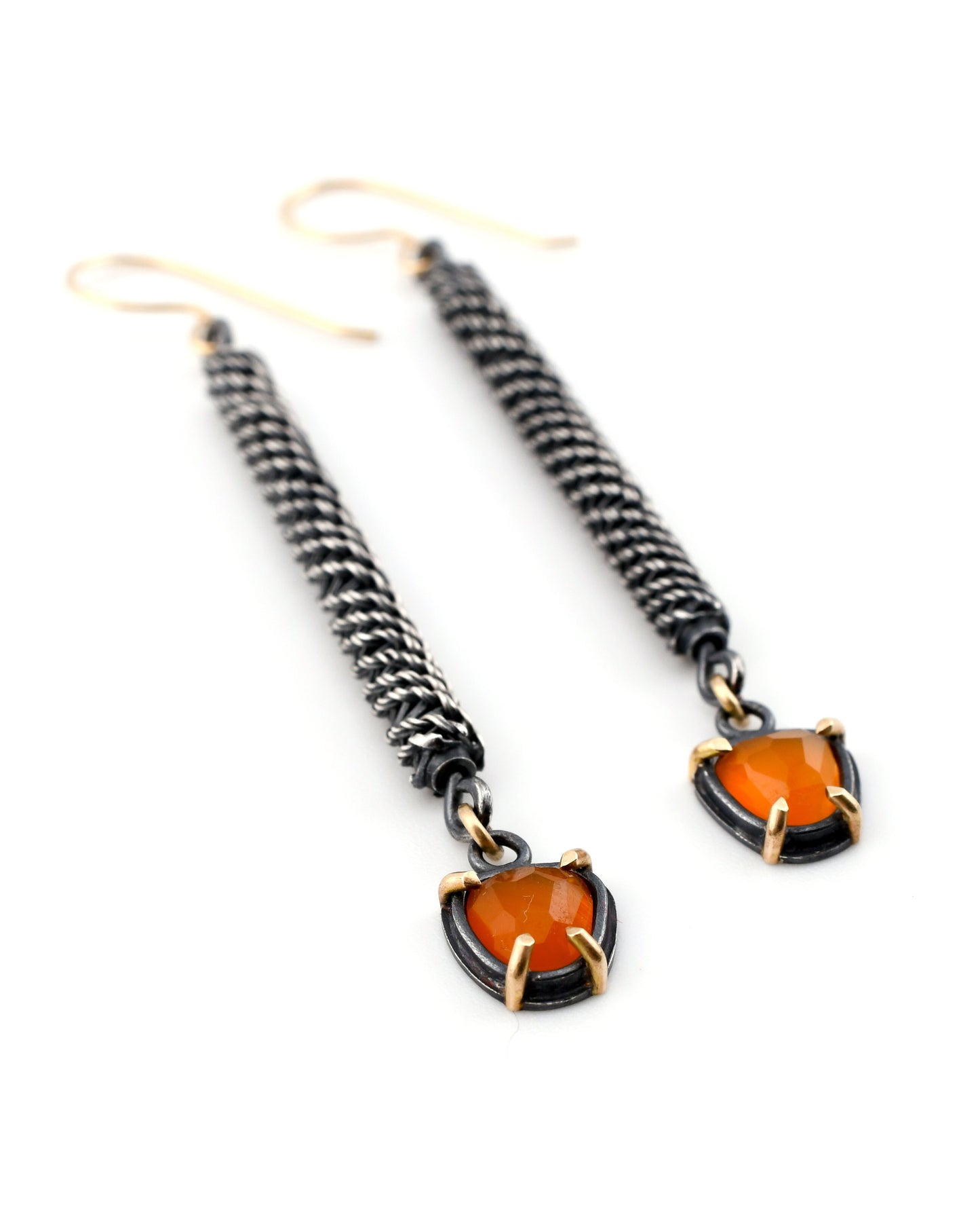 Pair of earrings with woven design and orange gemstones on a white background