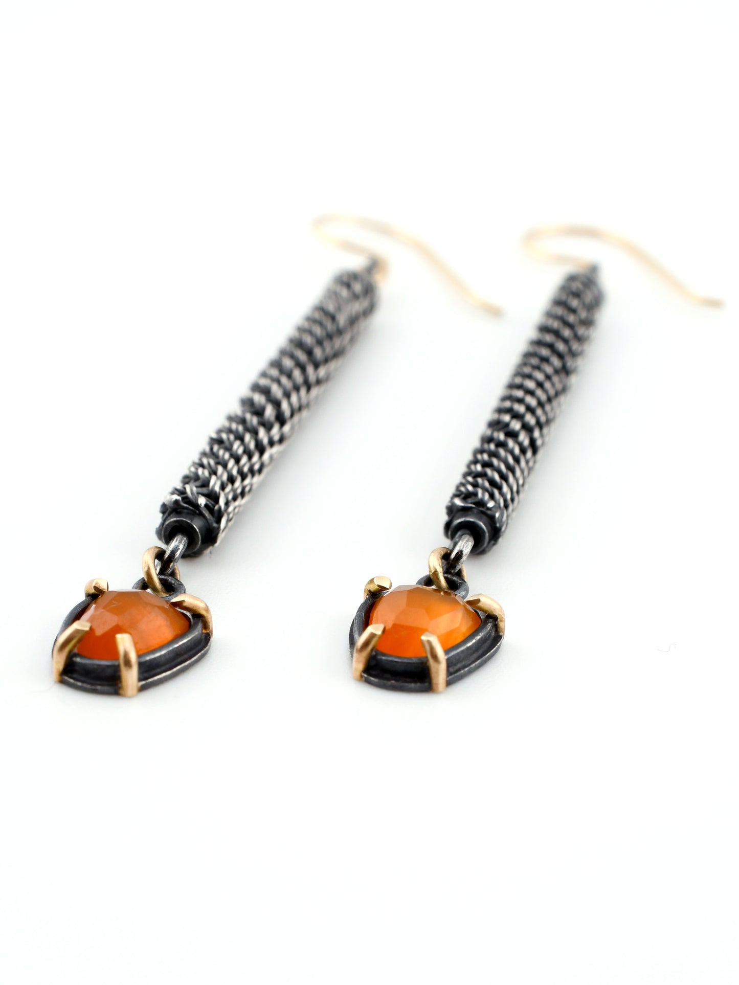 Pair of earrings with orange gemstones and black woven designs on a white background