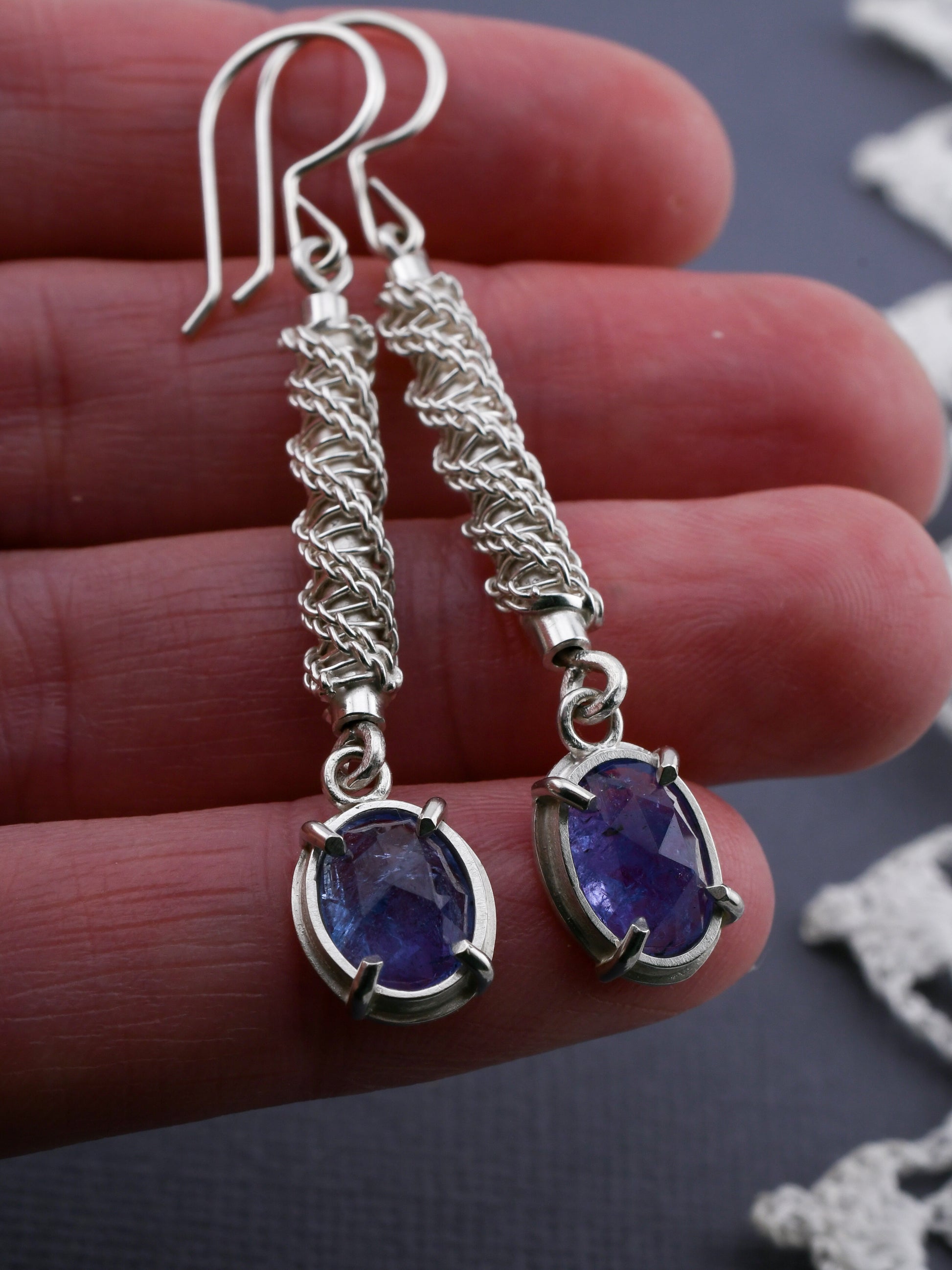 Silver earrings with purple gemstones held between fingers