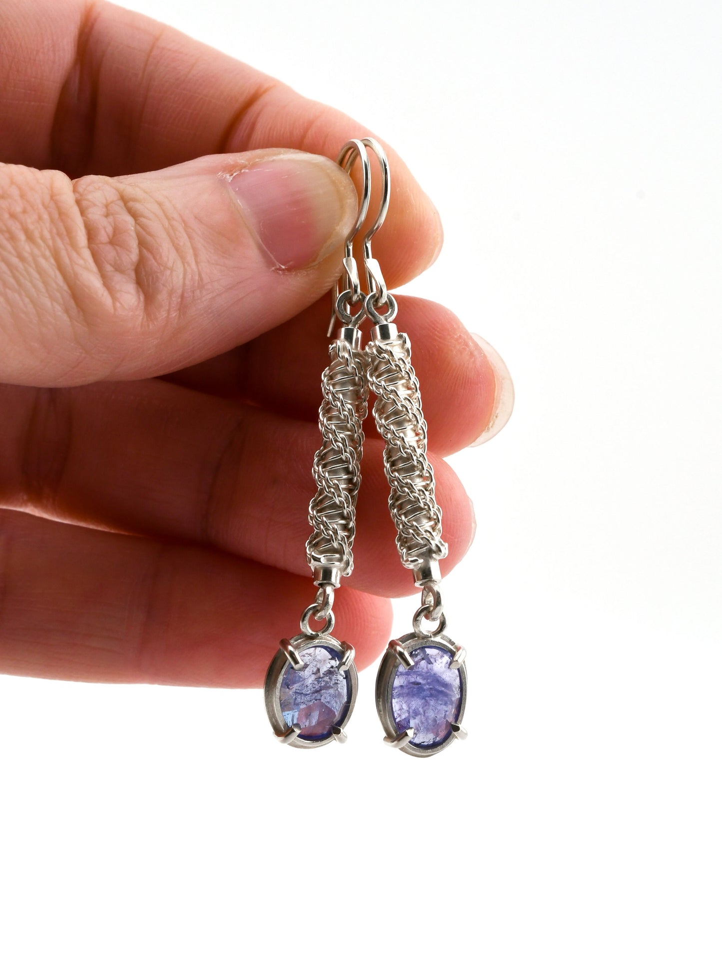 Silver earrings with purple gemstones held by a hand on a white background