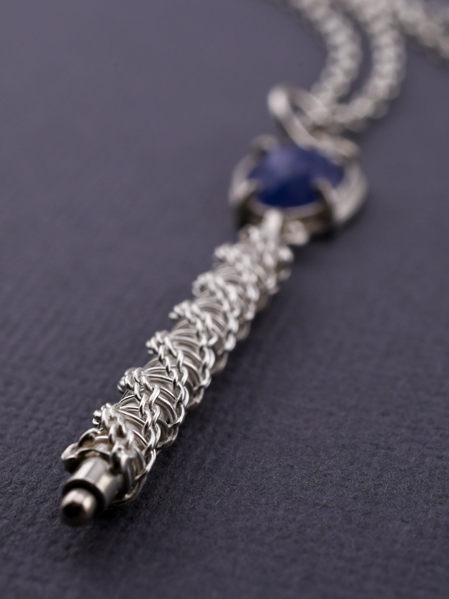 Silver necklace with a blue gemstone on a dark background