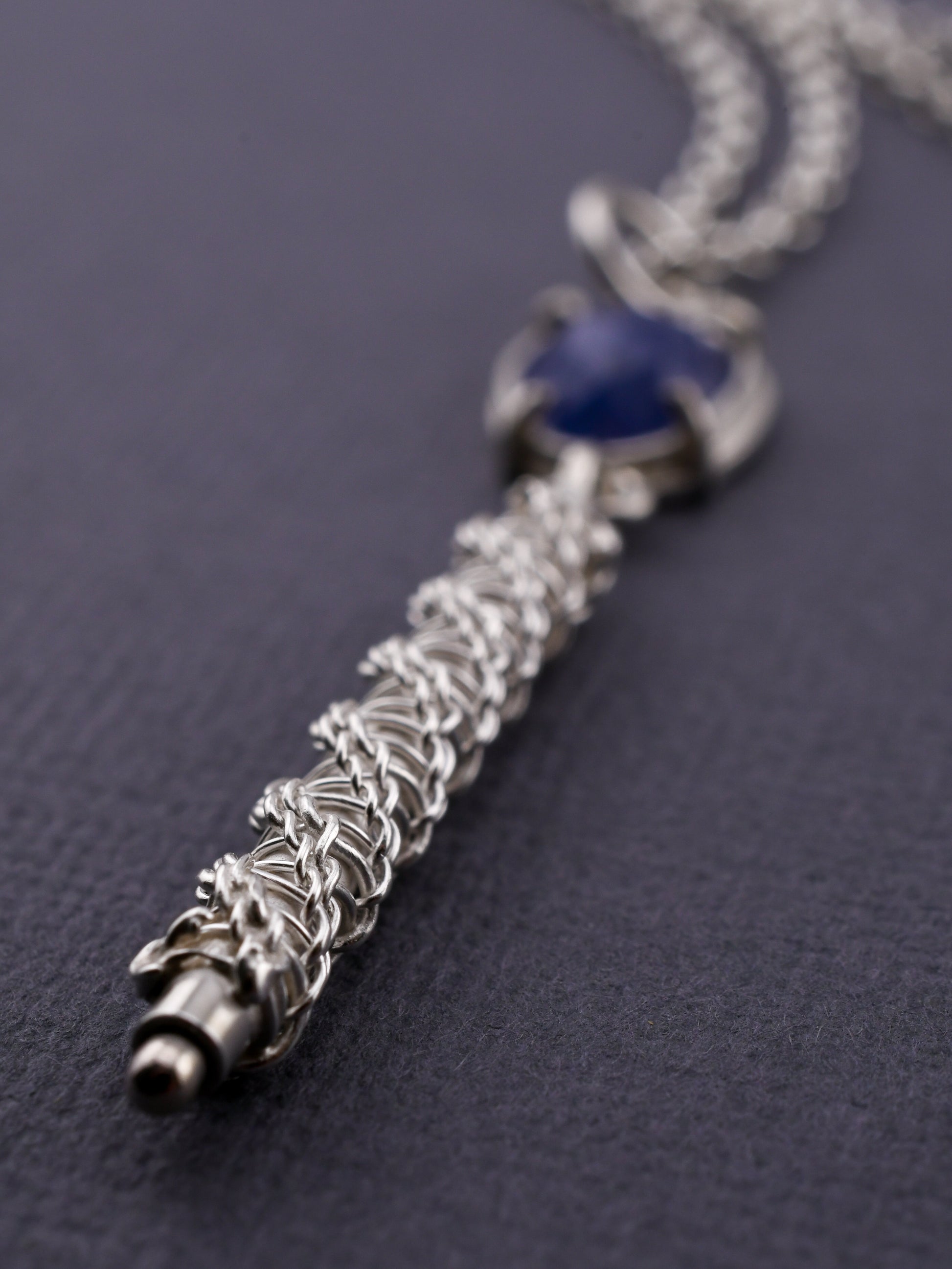 Silver necklace with a blue gemstone on a dark background