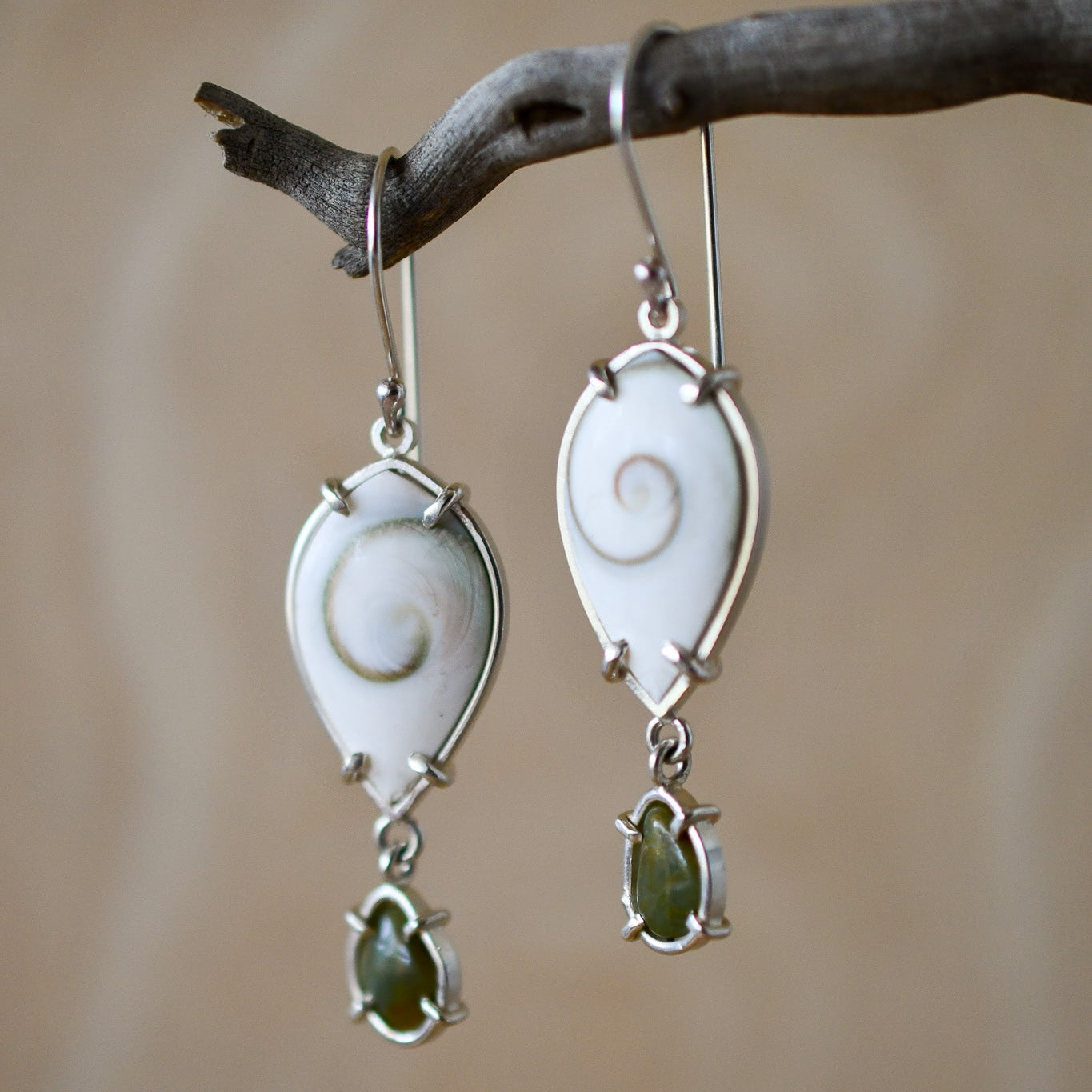 Pair of silver earrings with green stones hanging on a branch.