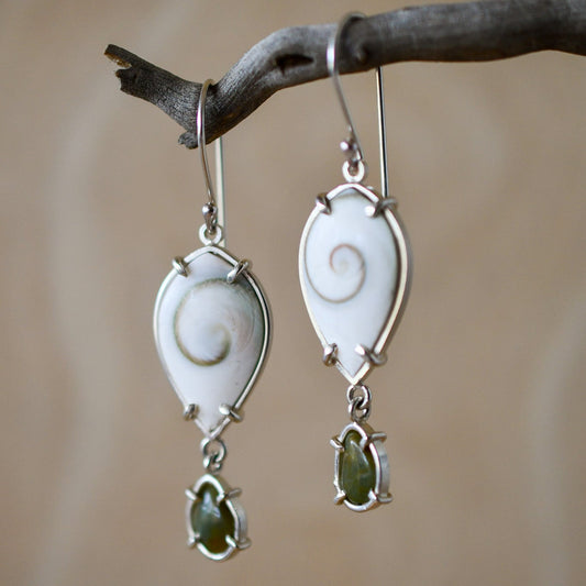 Pair of silver earrings with green stones hanging on a branch.