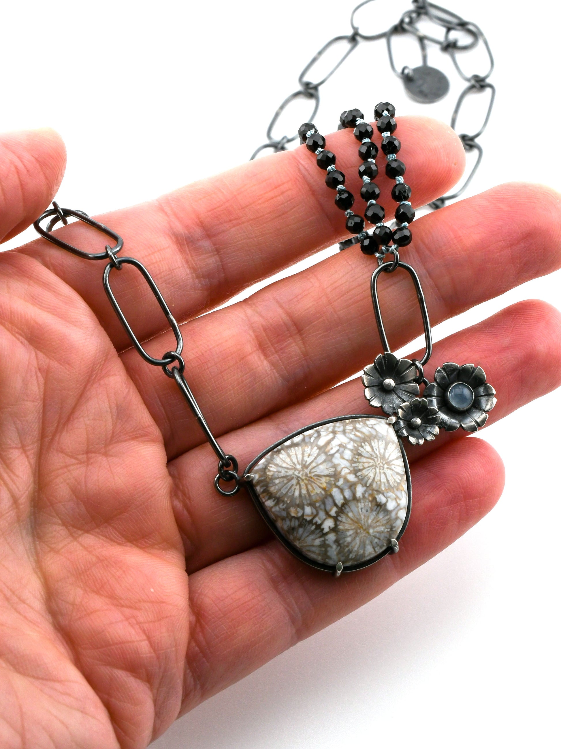 Necklace with floral pendant held in a hand against a white background