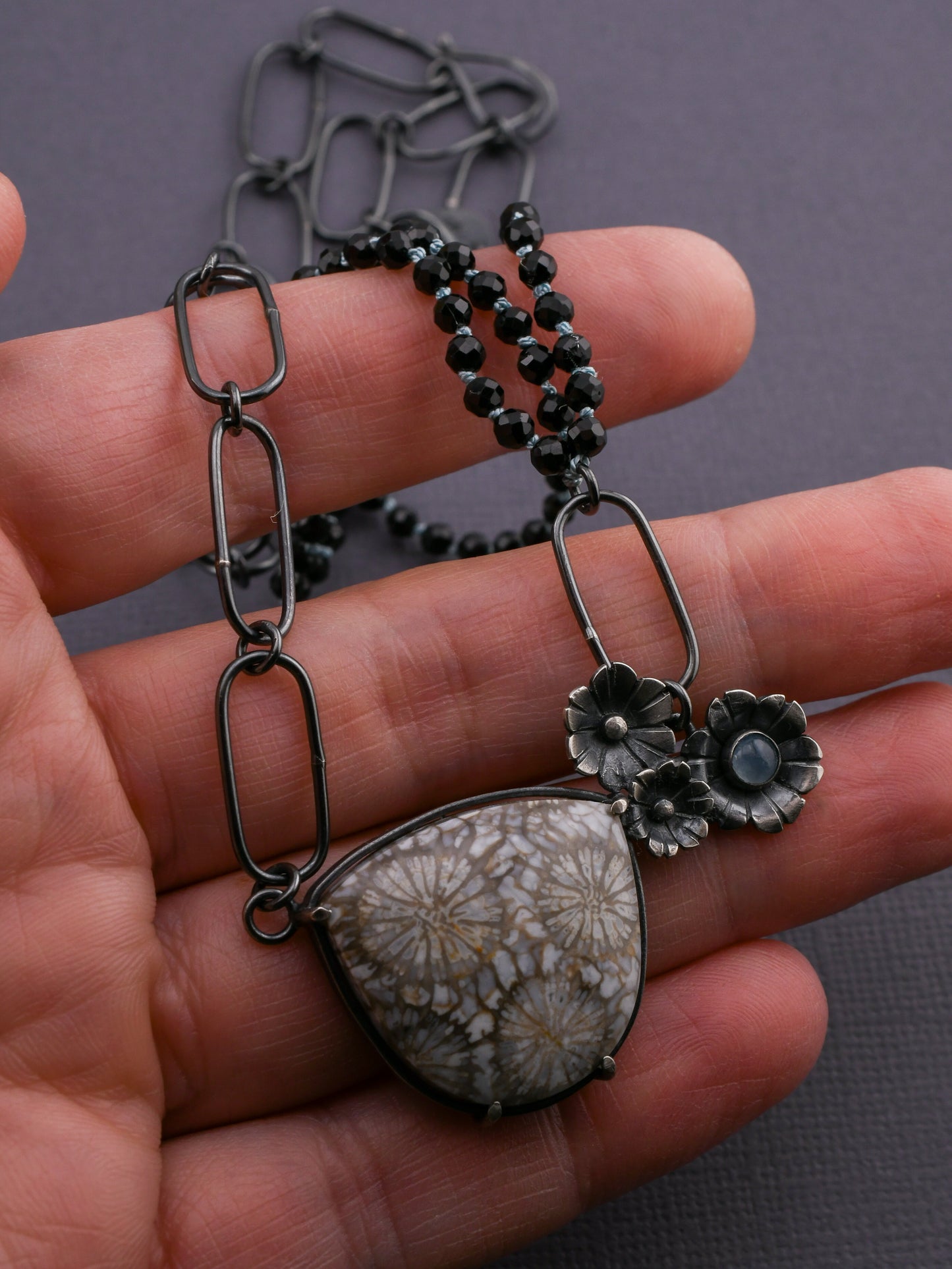 Necklace with floral pendant held in hand against a gray background