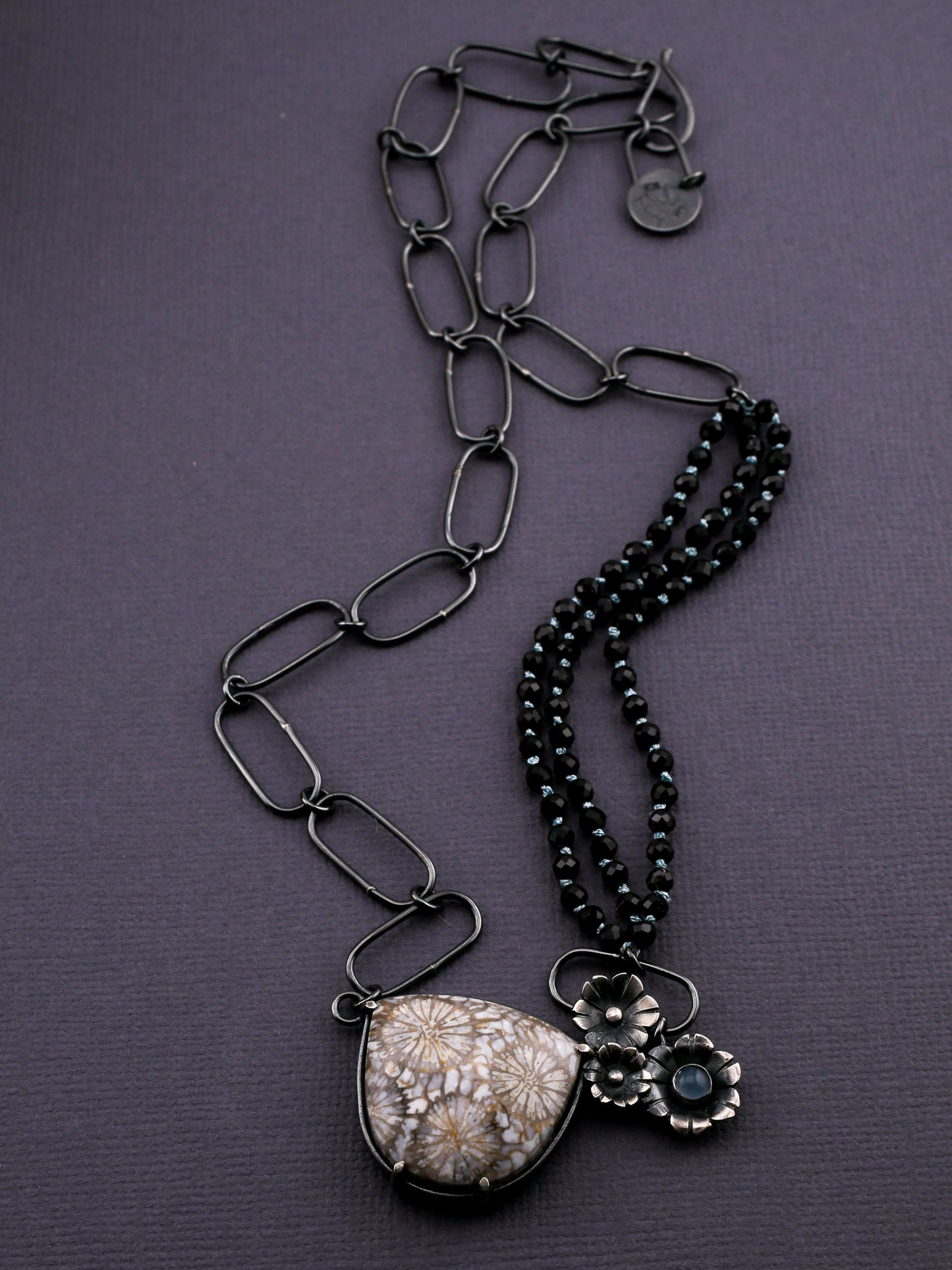 Black chain necklace with floral pendant on a purple background