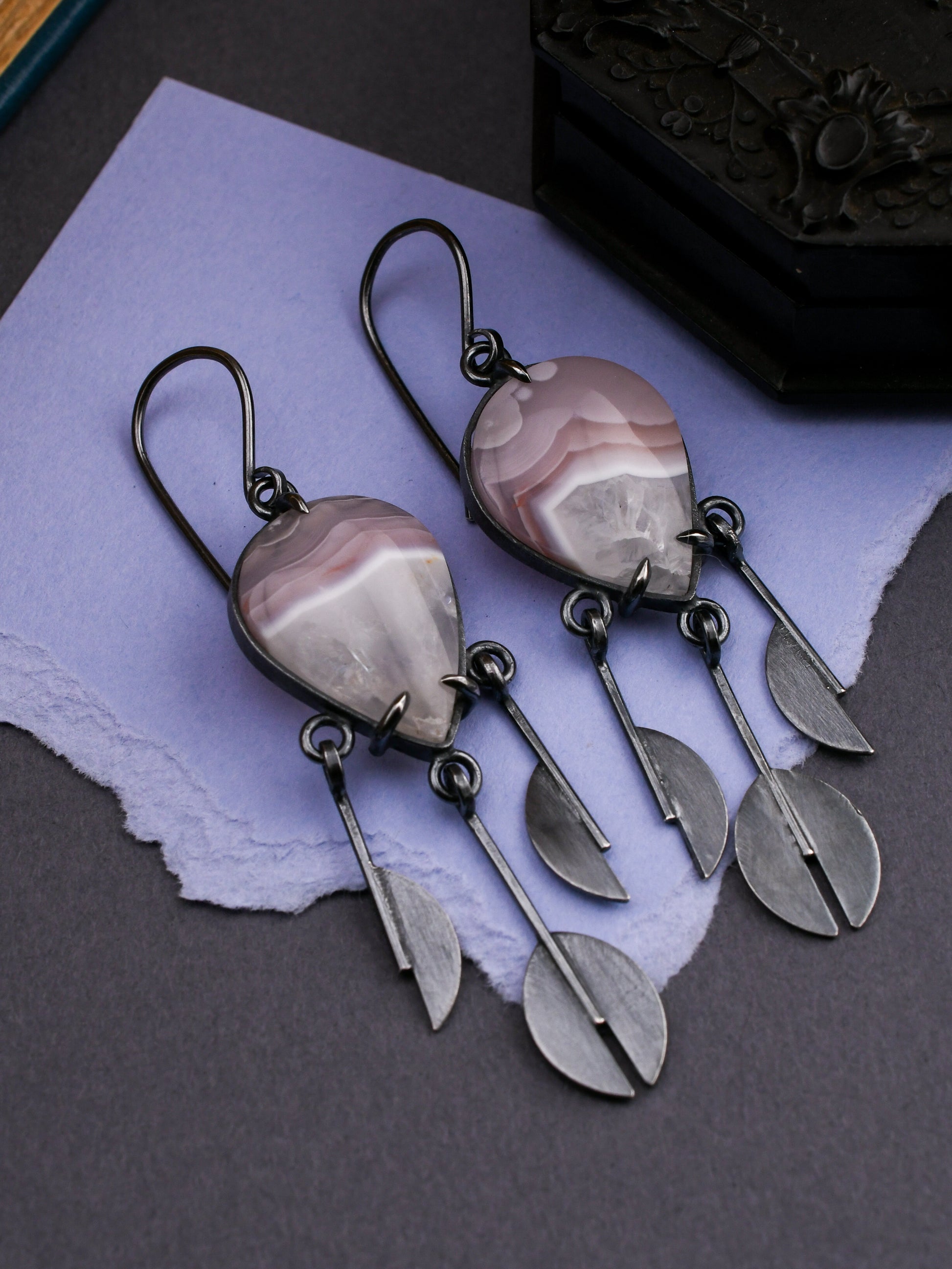Pair of earrings with pink and lavender stones and silver rain pendants on a purple fabric background.