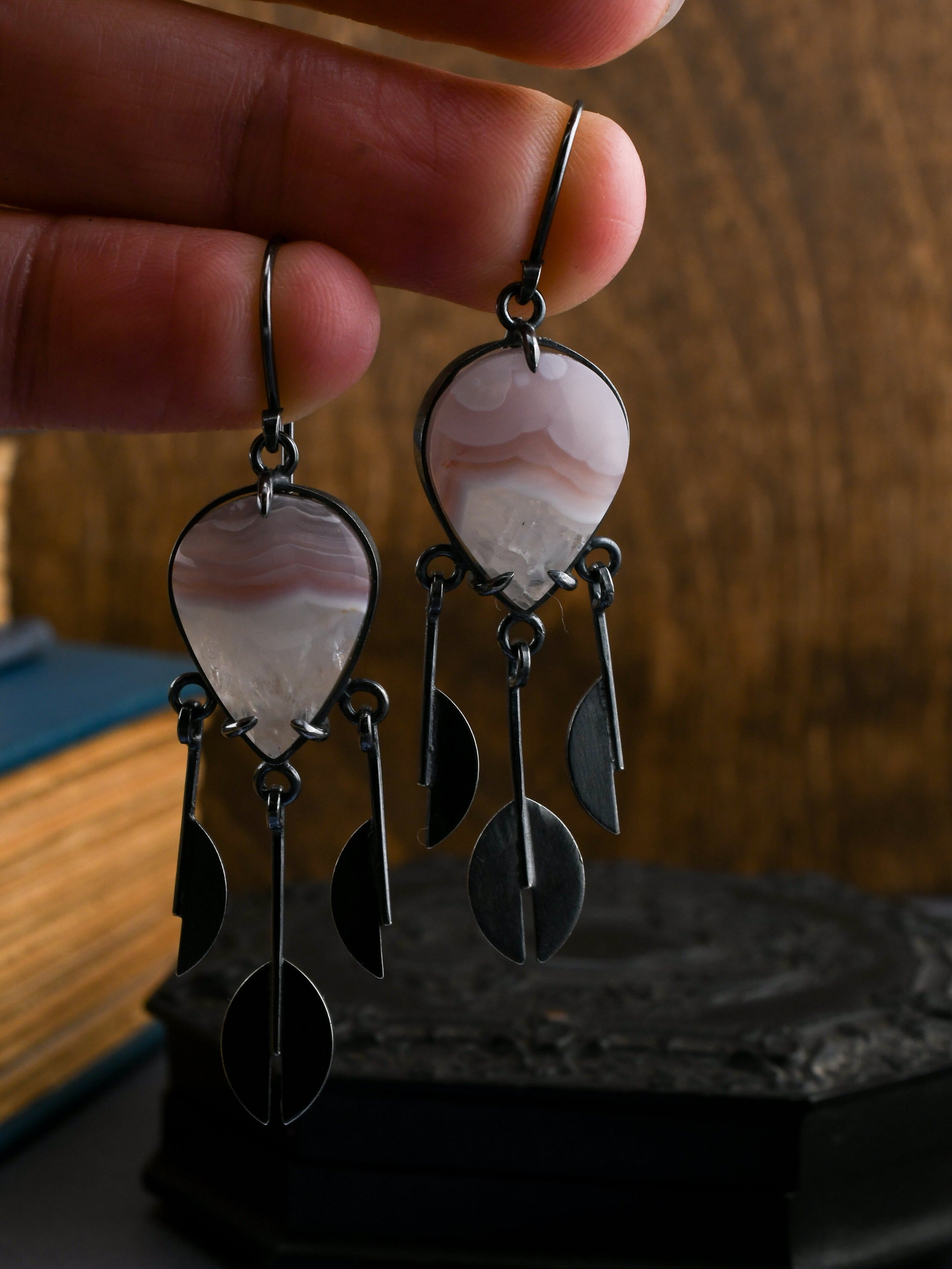 Pair of agate earrings held in a hand over a dark background with books and an ornate box