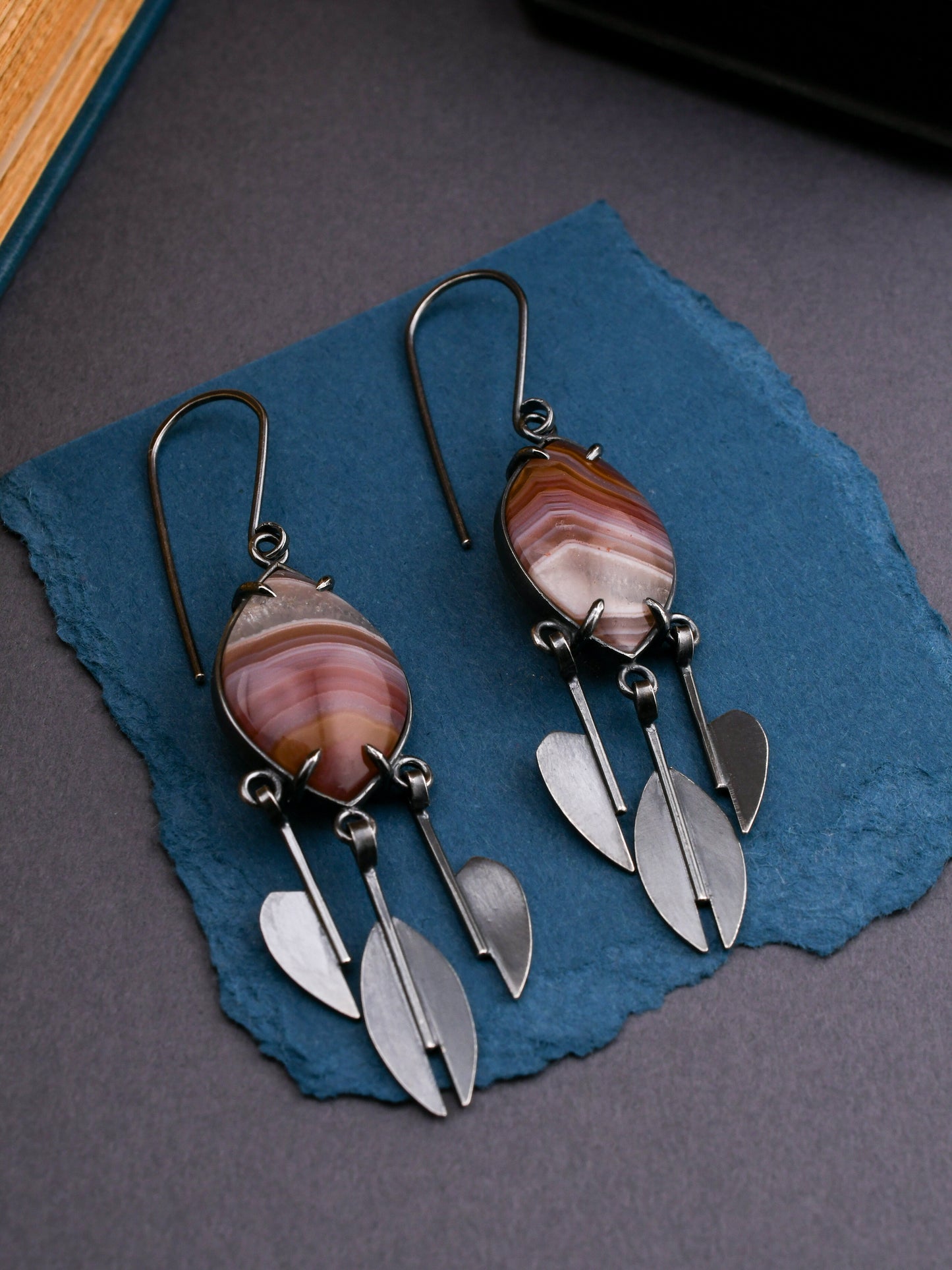 Pair of earrings with agate stones and silver raindrop accents on a blue stone surface.