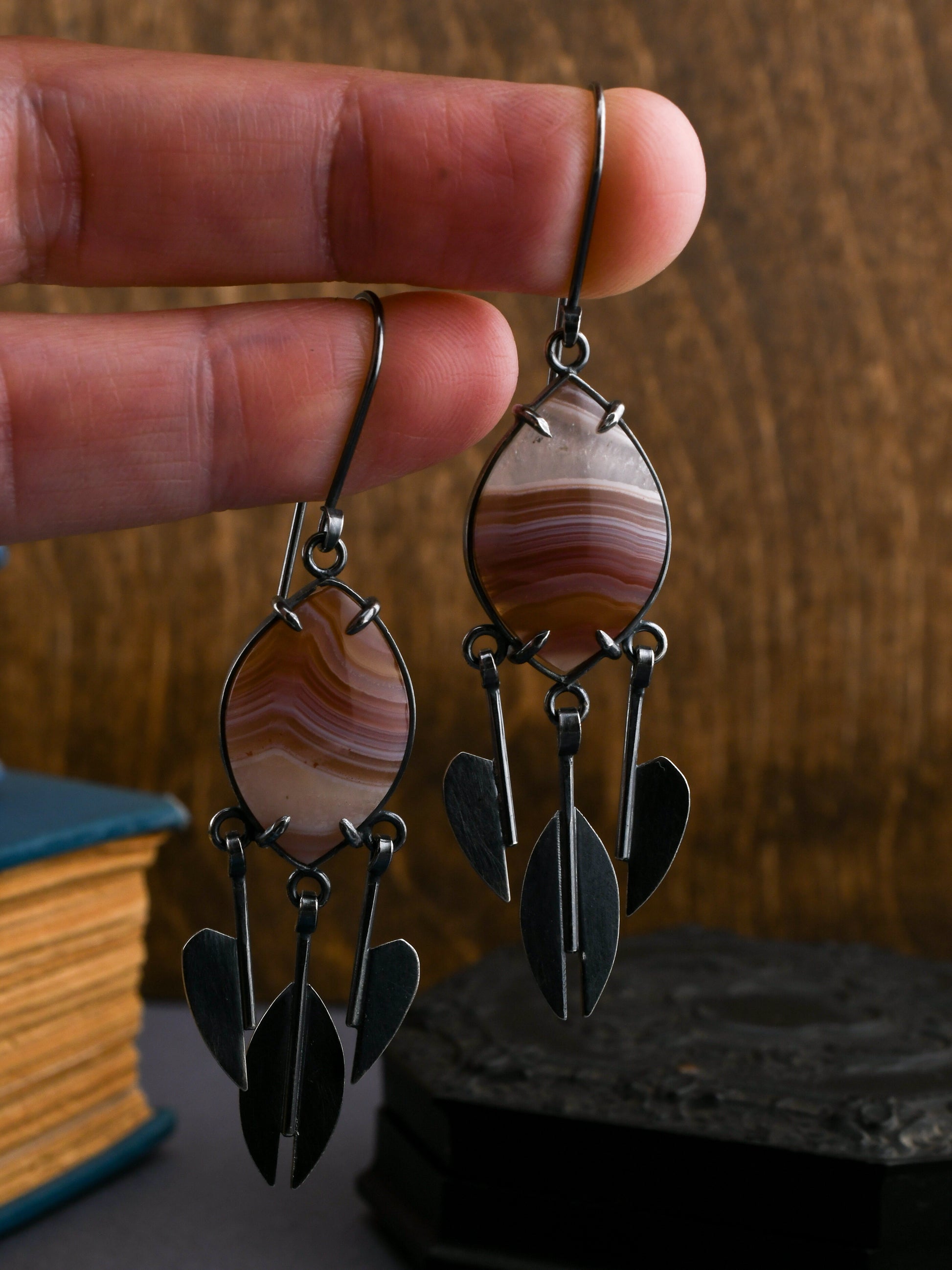 Pair of earrings with banded agates held between fingers against a wooden background