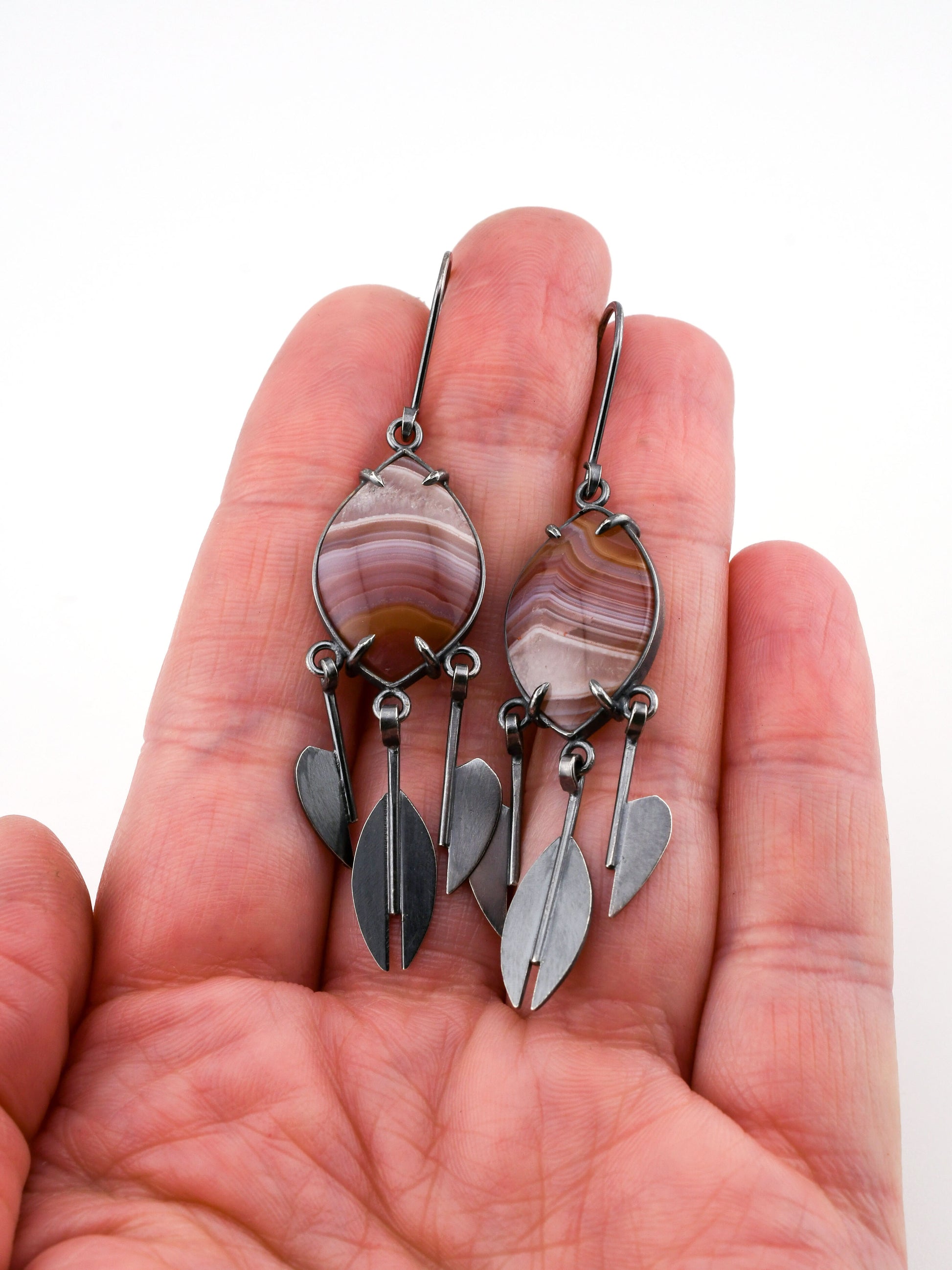 Pair of silver and stone earrings held in a hand against a white background