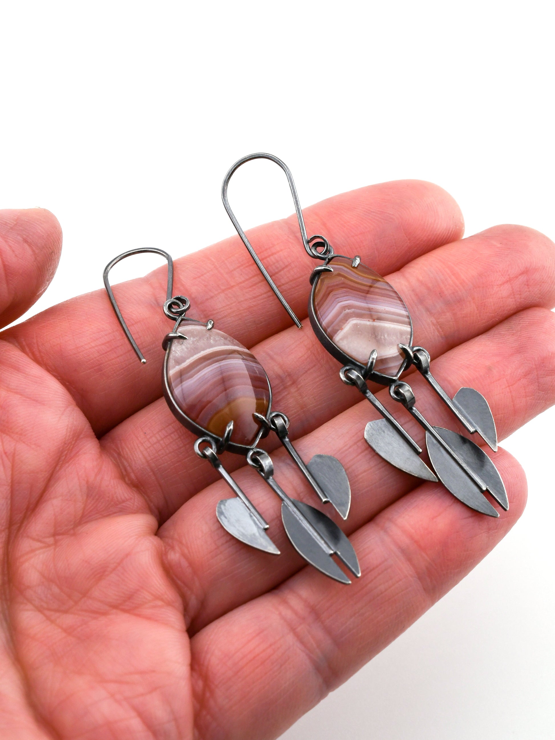 Hand holding a pair of silver and stone earrings on a white background