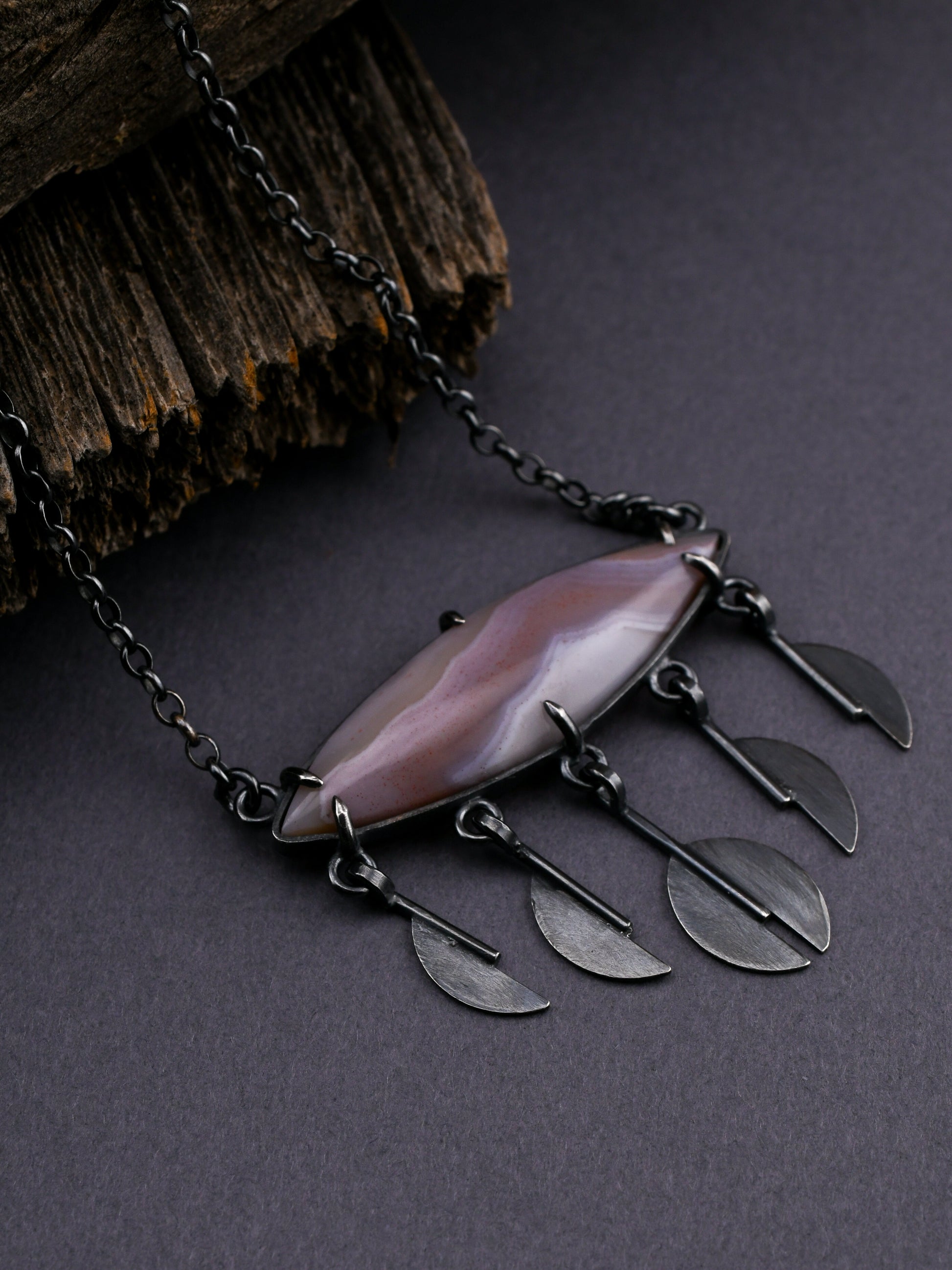 Necklace with a large pendant and stylized raindrop elements on a dark background