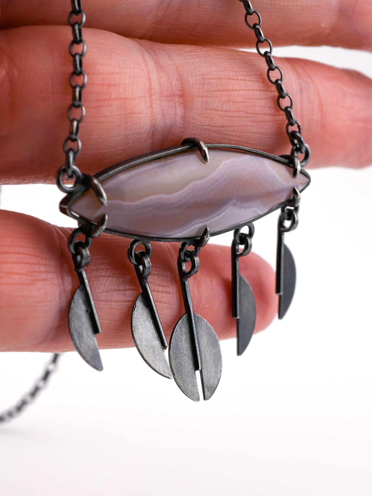 Necklace with a large stone pendant and raindrop pendants held between fingers.