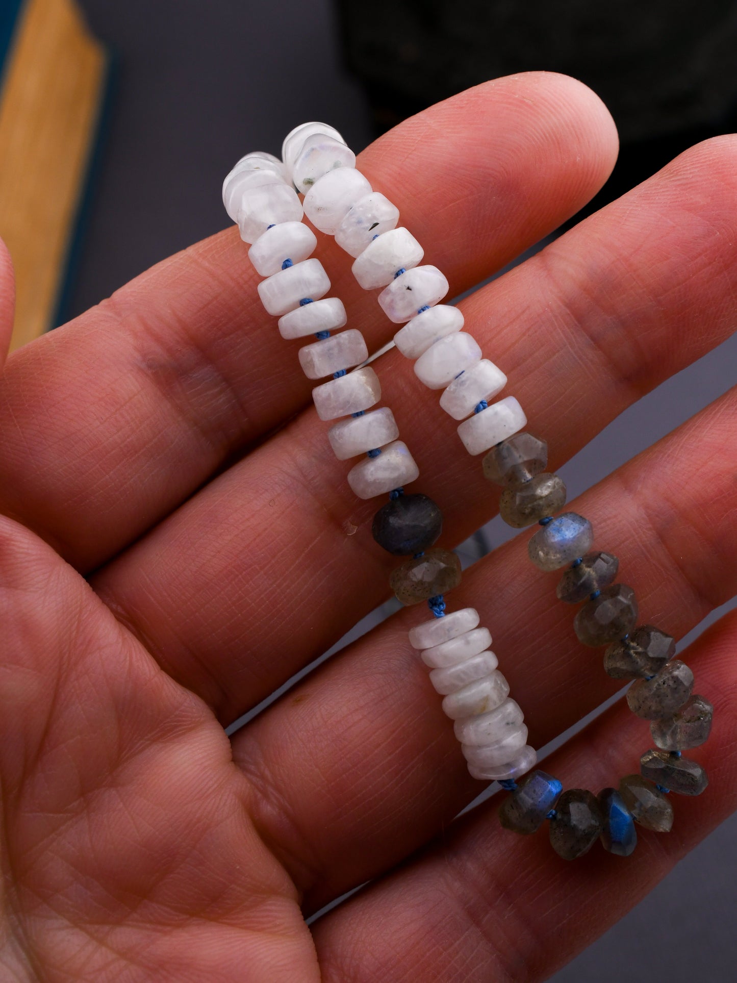 hand holding beaded necklace with white and gray stones over a dark background