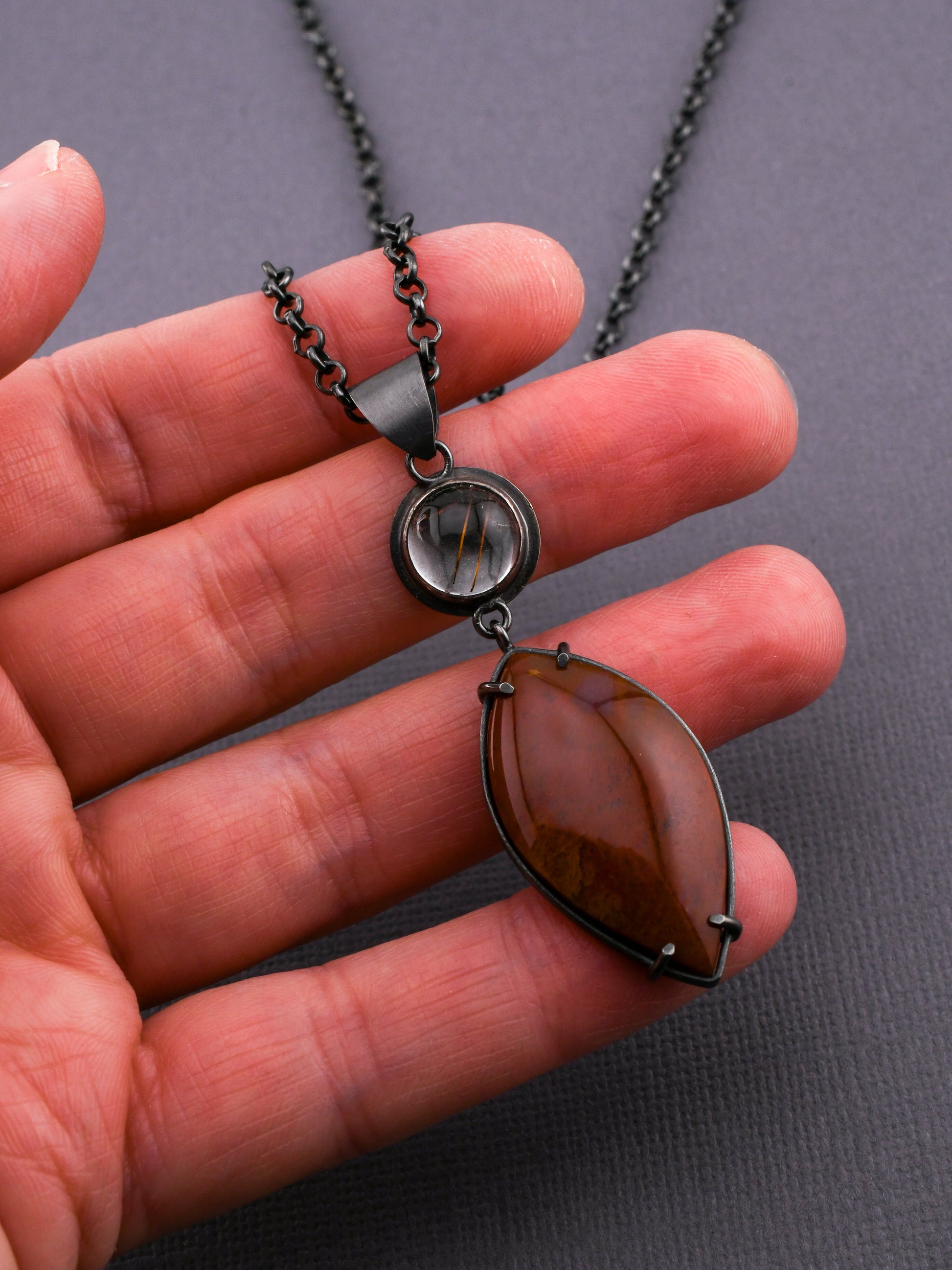 Necklace with a pendant held in a hand against a gray background