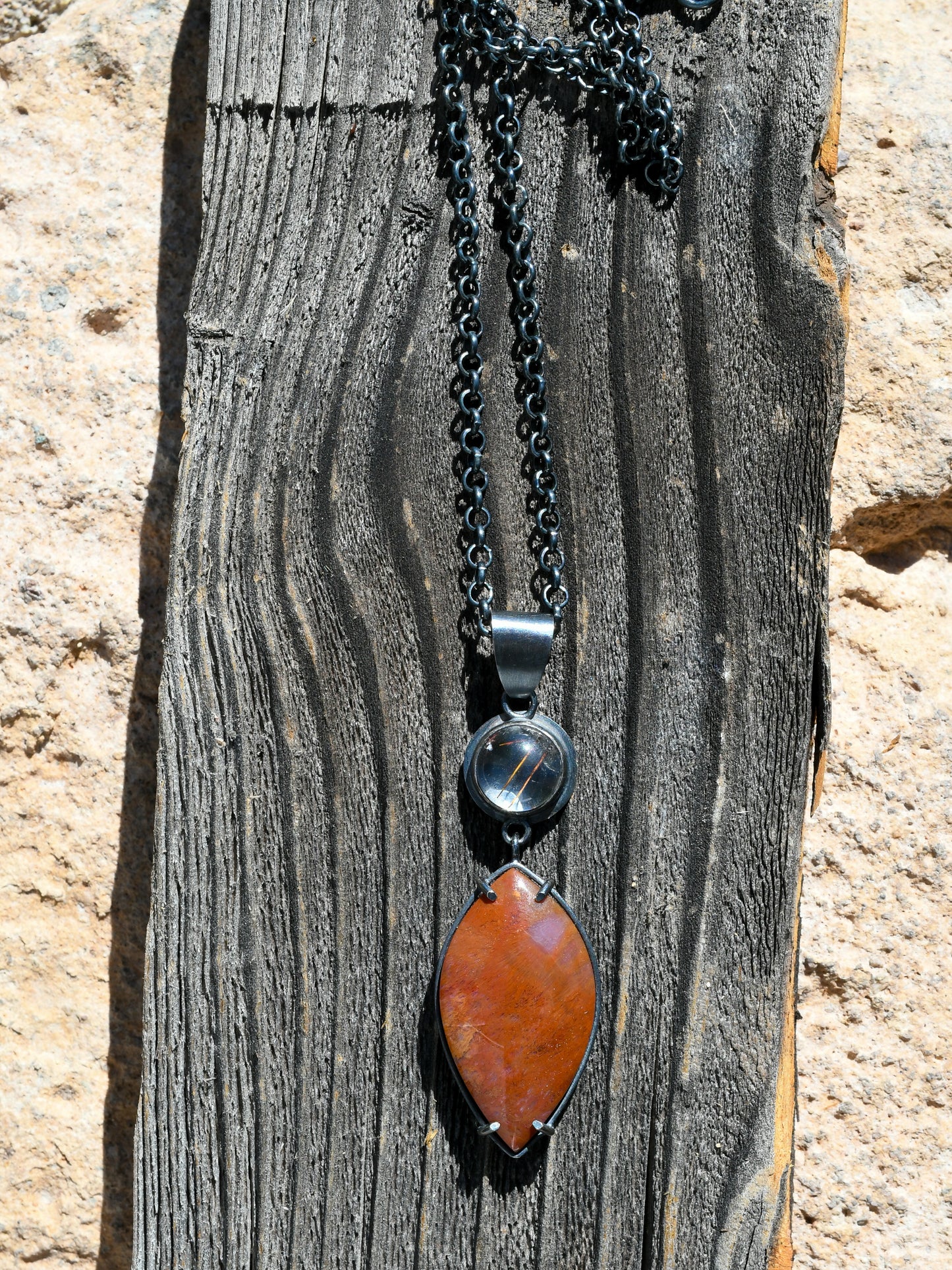 Necklace with a red pendant and black chain on a wooden surface
