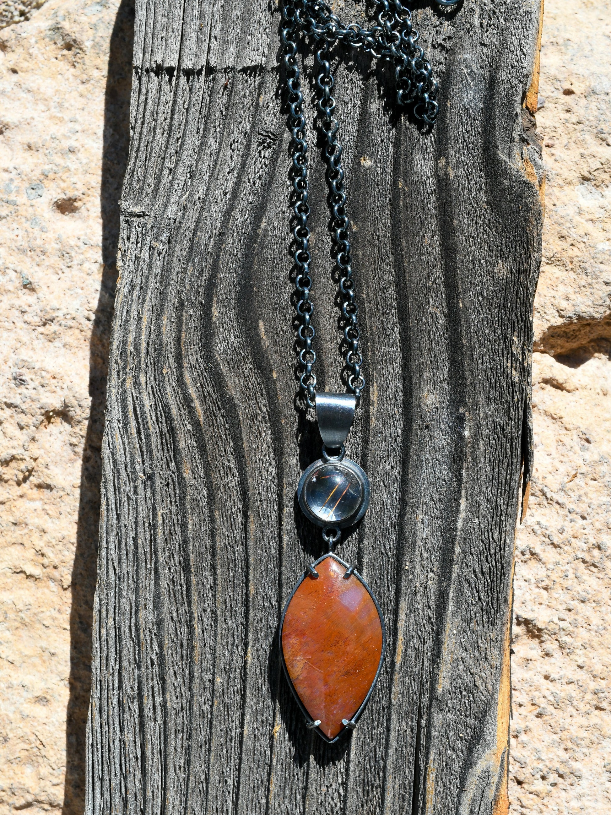 Necklace with a red pendant and black chain on a wooden surface