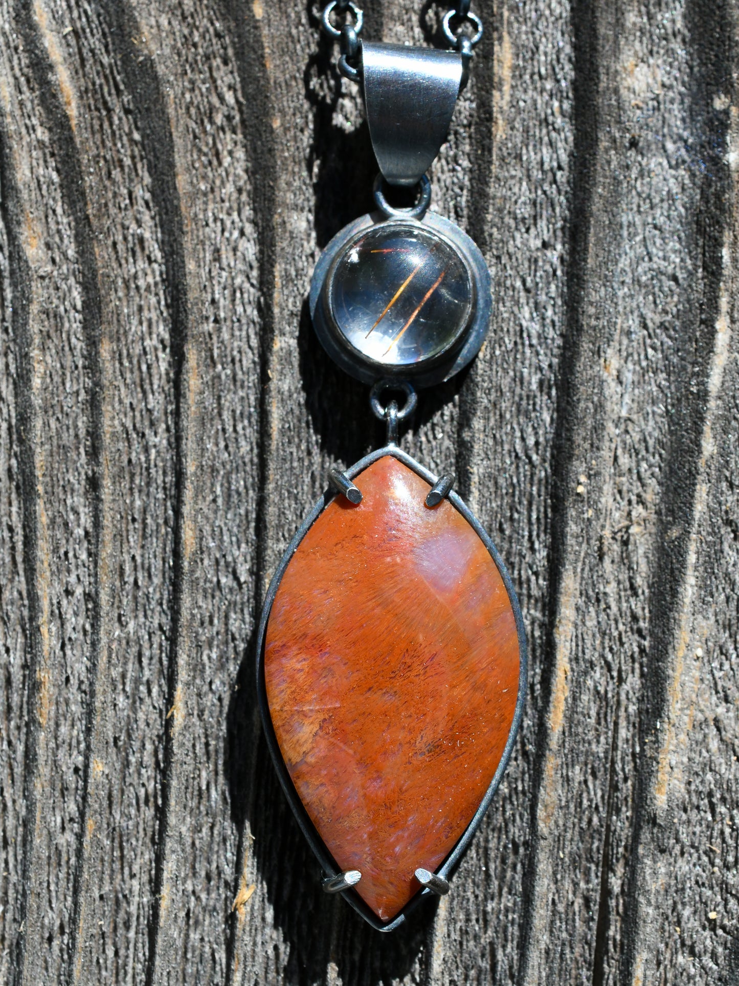 Necklace with a red pendant and black chain on a wooden surface