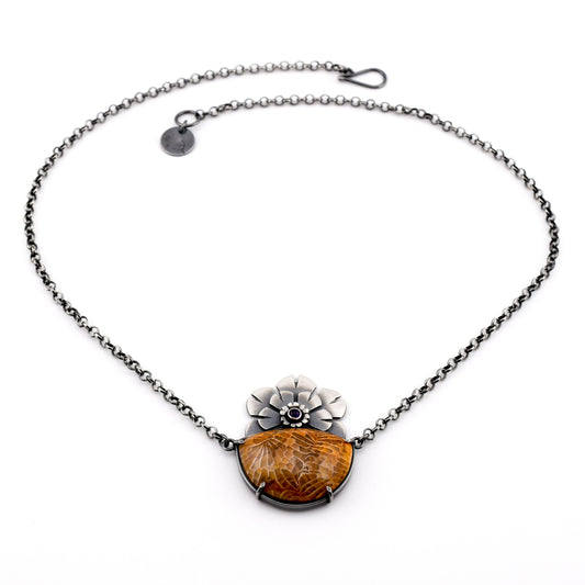 silver necklace with golden ochre fossilized coral and purple amethyst with stylized flowers arranged in a circle on a white surface