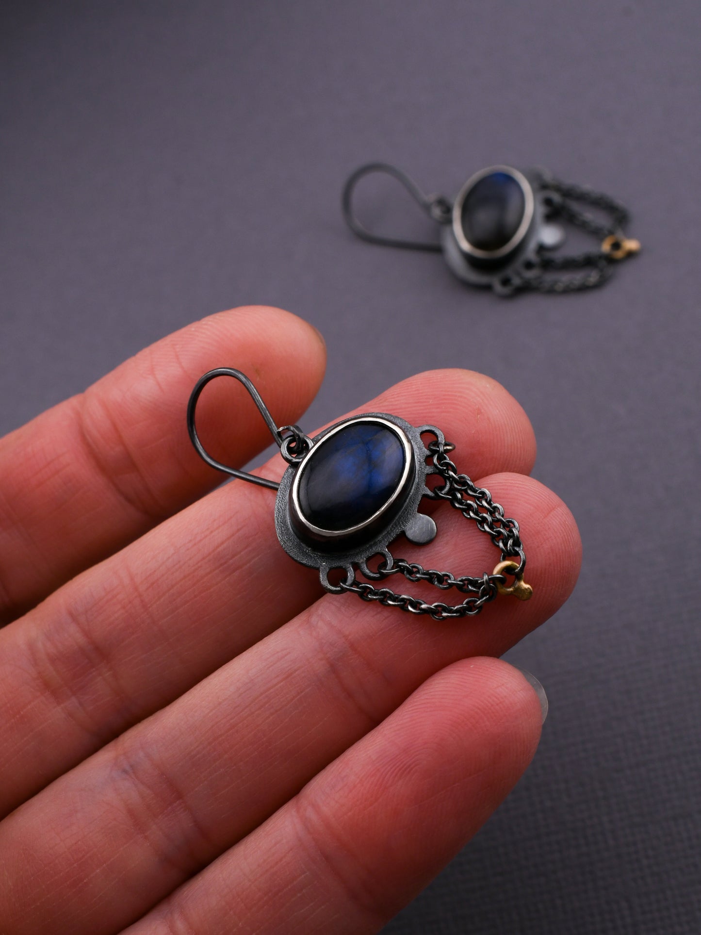 Earring with blue gemstone held in a hand against a dark background