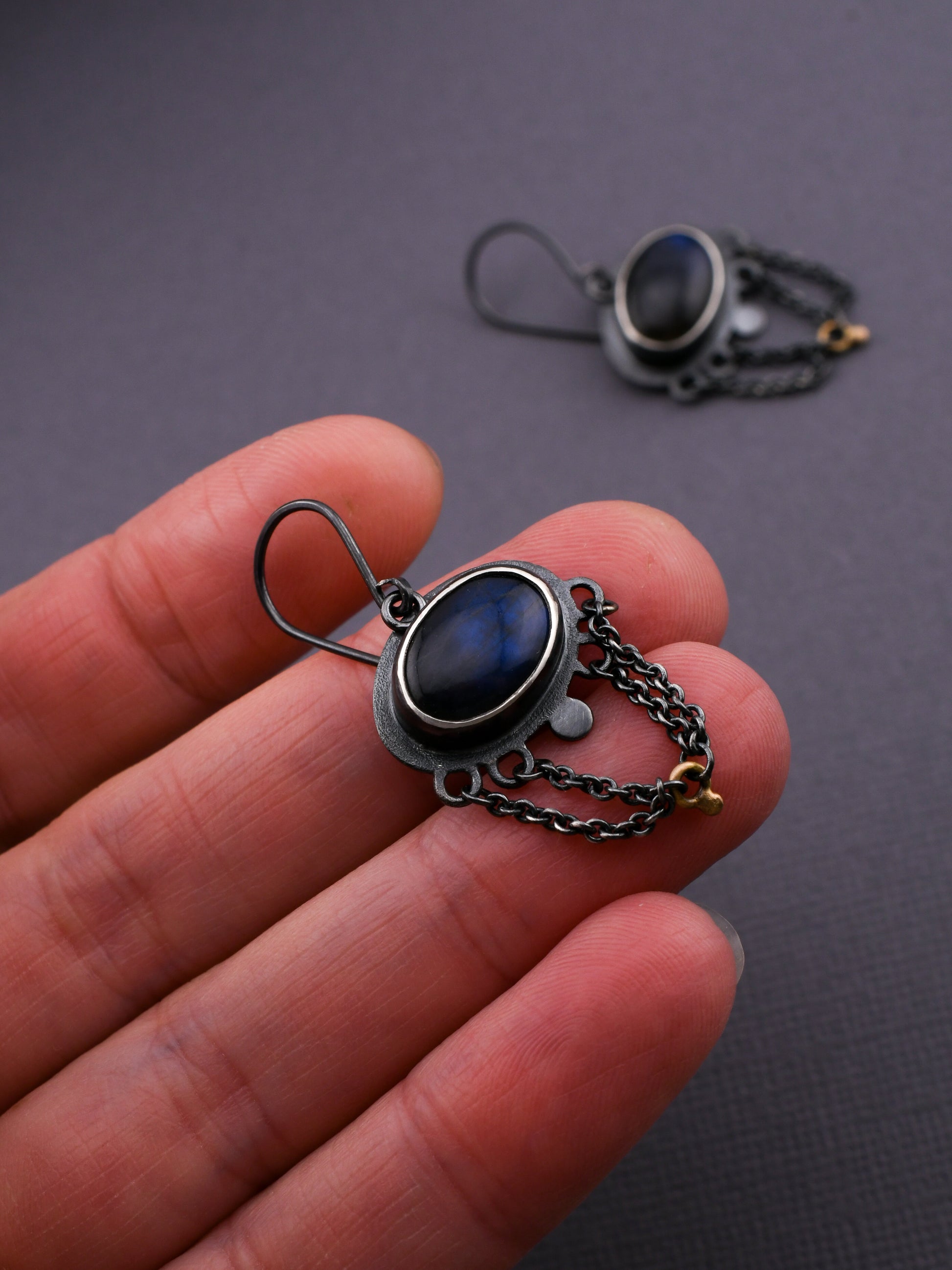 Earring with blue gemstone held in a hand against a dark background